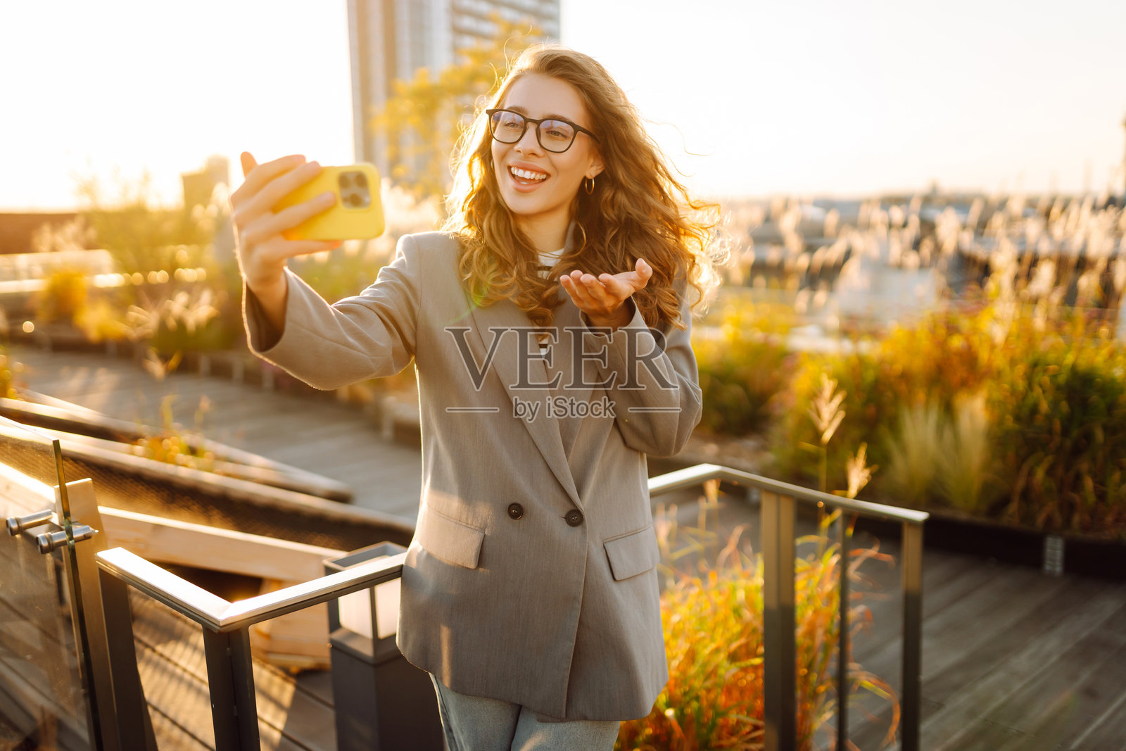 一位时尚女性戴着眼镜，手持手机，站在阳光明媚的屋顶上拍摄的肖像。照片摄影图片