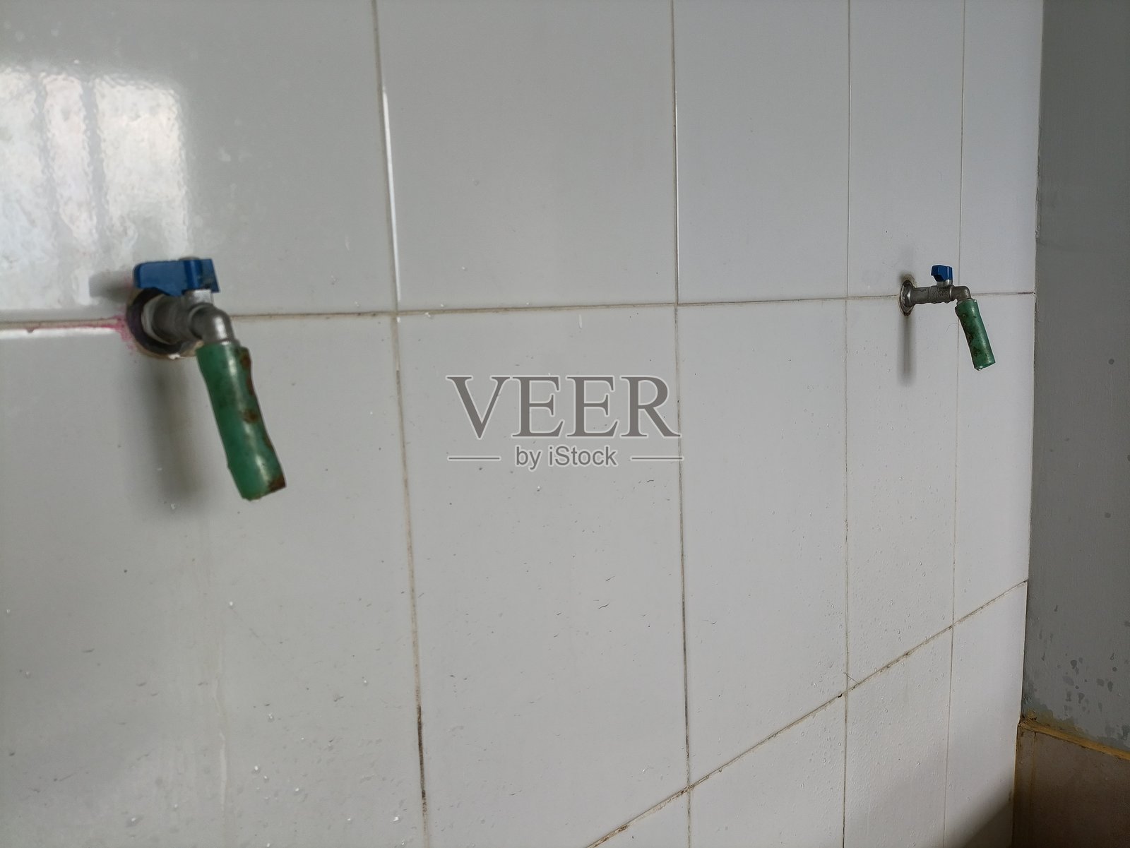 两人使用的洗手台区域，配有2个水龙头。墙壁铺有白色陶瓷瓷砖，并设有集水槽。照片摄影图片