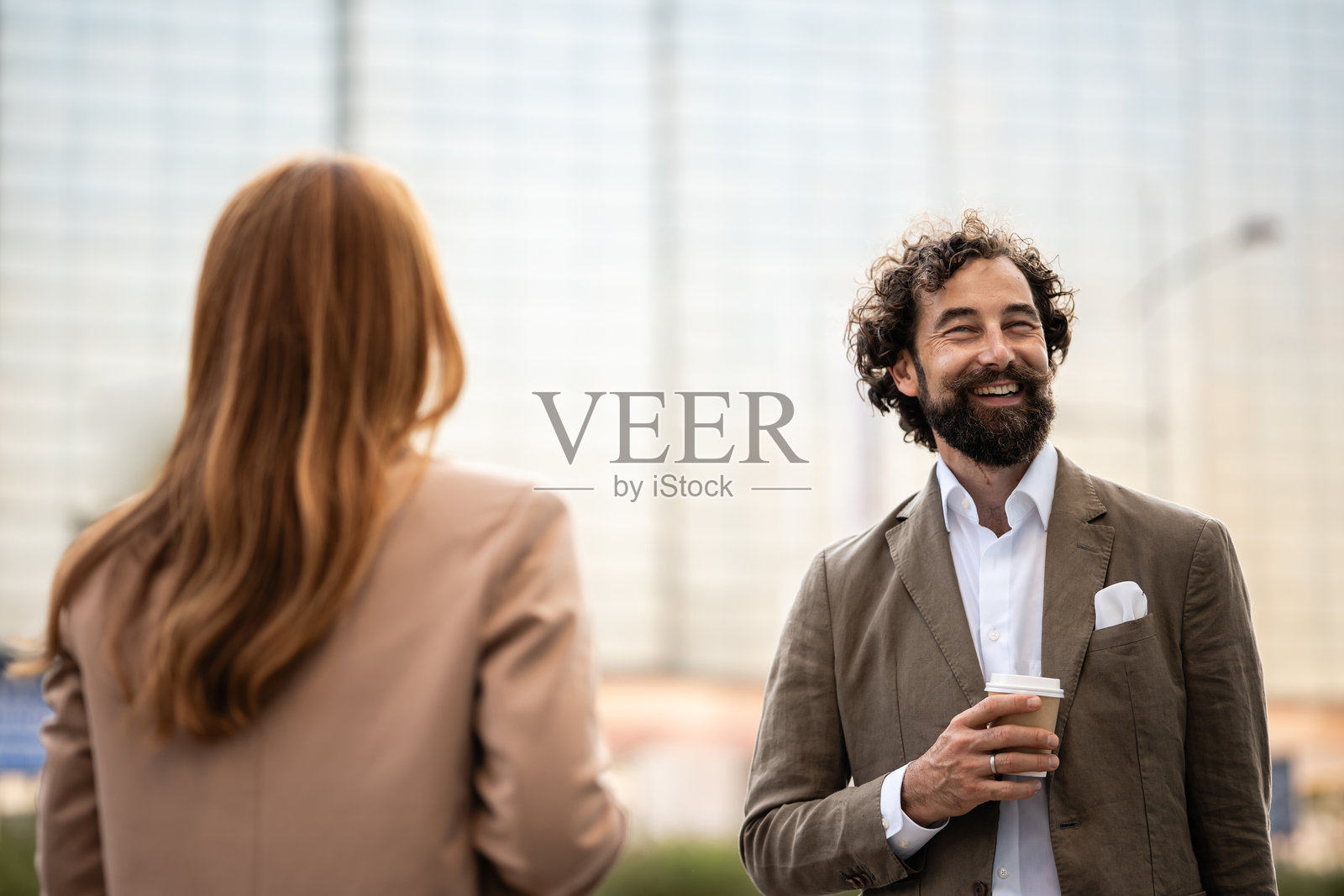 一位面带微笑的商人在户外拿着咖啡与女同事交谈照片摄影图片