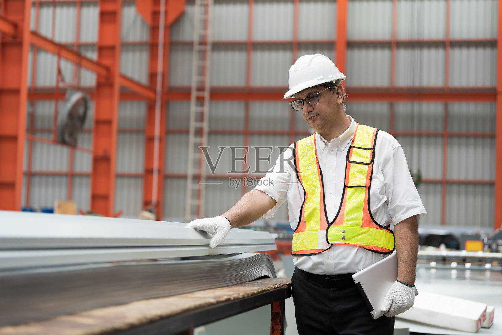 工厂男工人在工厂检查镀锌屋顶或金属板的质量。男工人在工厂生产流程后，在仓库中检查金属板。照片摄影图片