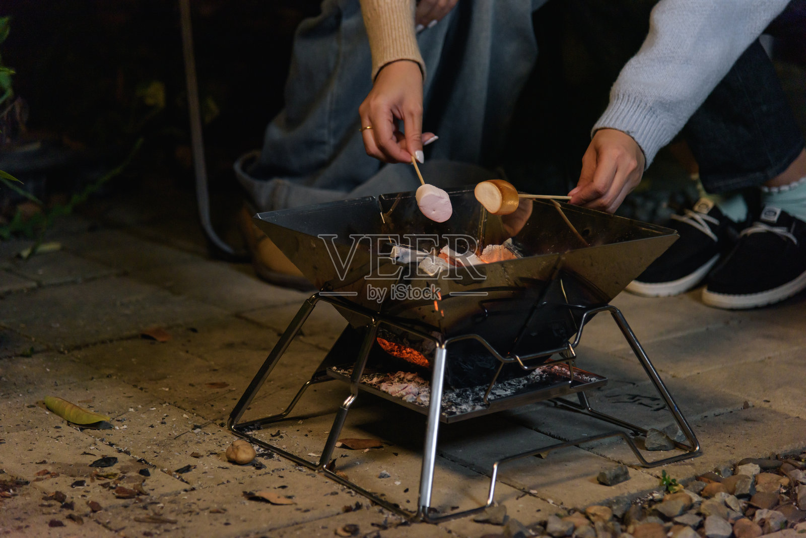 快乐的女性朋友们在户外森林营地享受冬日活动，围坐在温暖的火坑旁烤棉花糖，在凉爽的冬夜里分享温暖。照片摄影图片