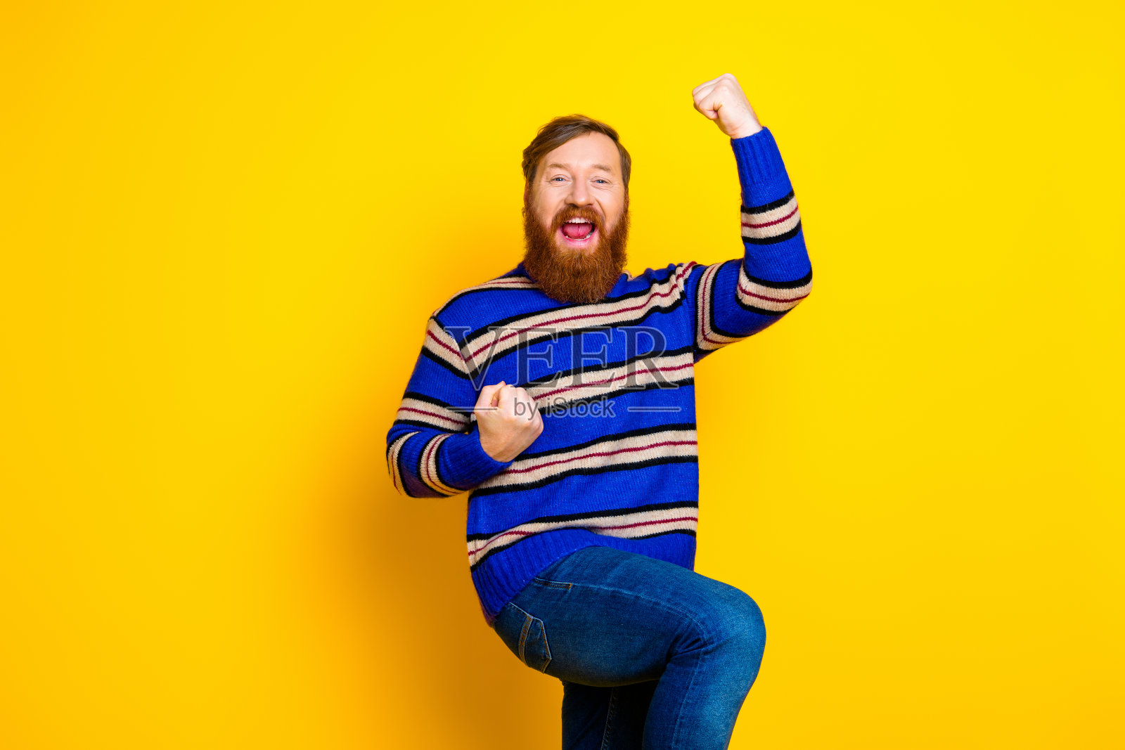一个留着红头发和胡须的年轻男子，穿着条纹毛衣，在充满活力的黄色背景前充满活力地摆姿势。照片摄影图片