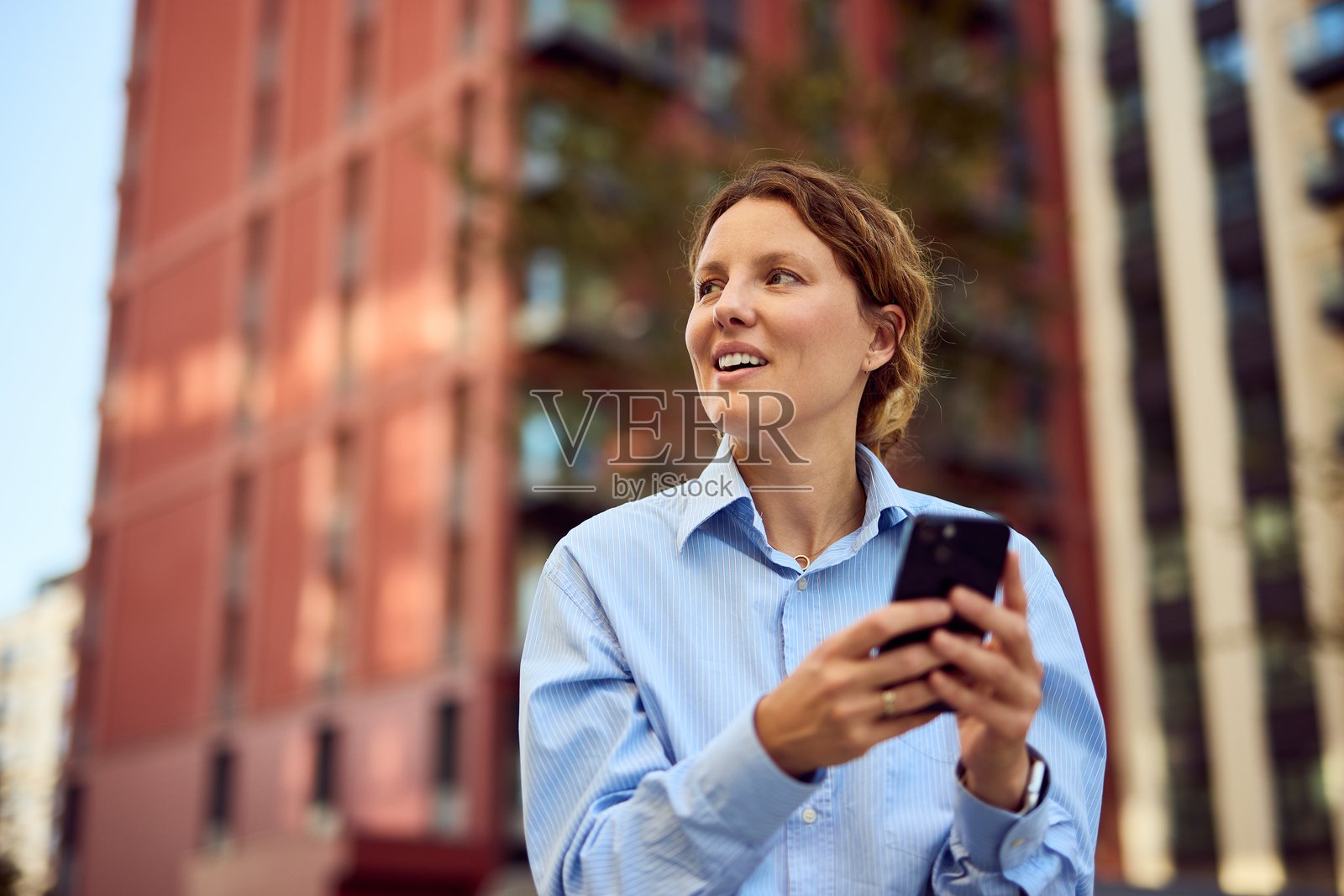 自信的商界女性在现代都市环境中边走边查看她的智能手机照片摄影图片