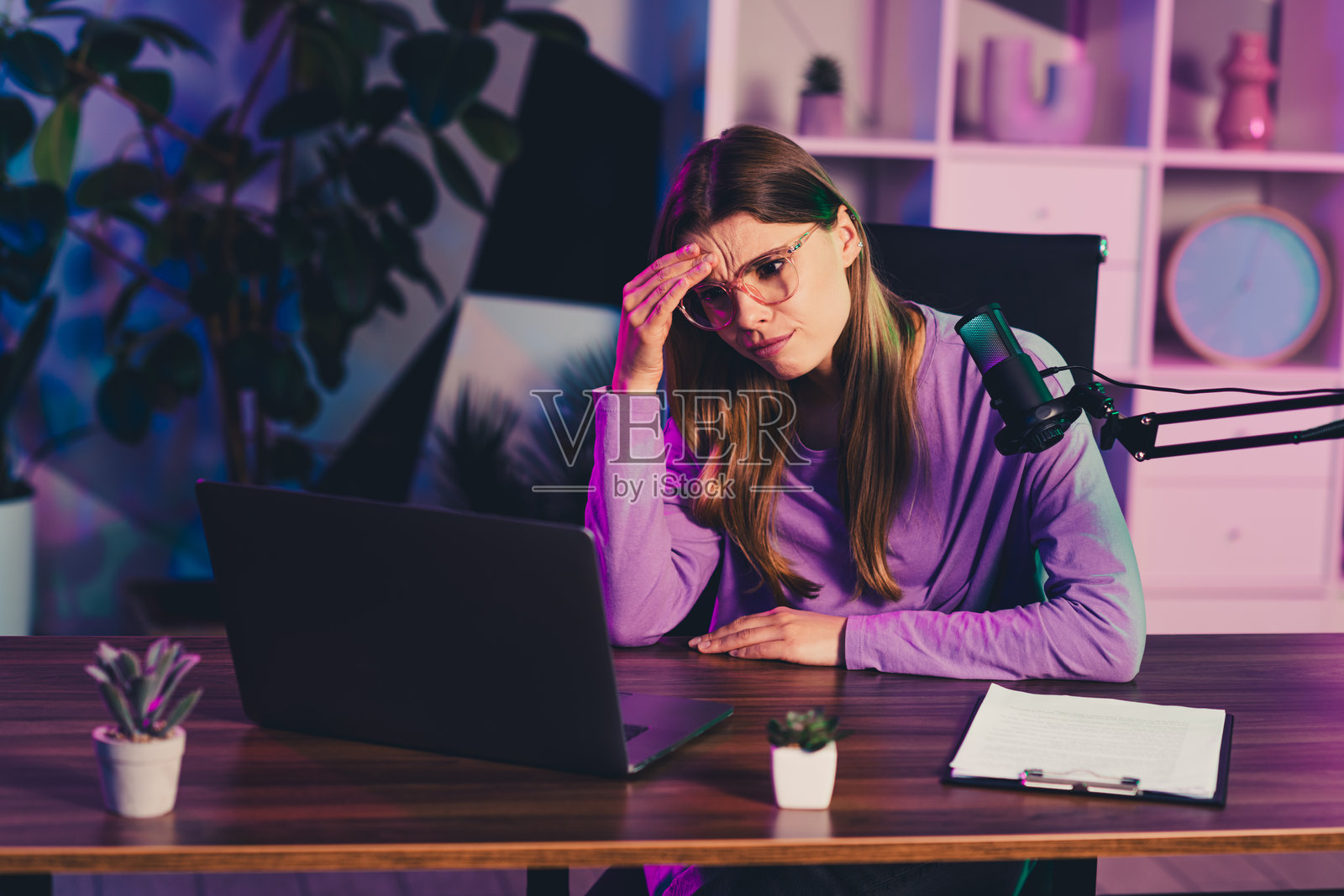 年轻的女博主，穿着休闲风格，在晚间灯光下，在家里的书桌前，使用麦克风和笔记本电脑进行内容直播。照片摄影图片