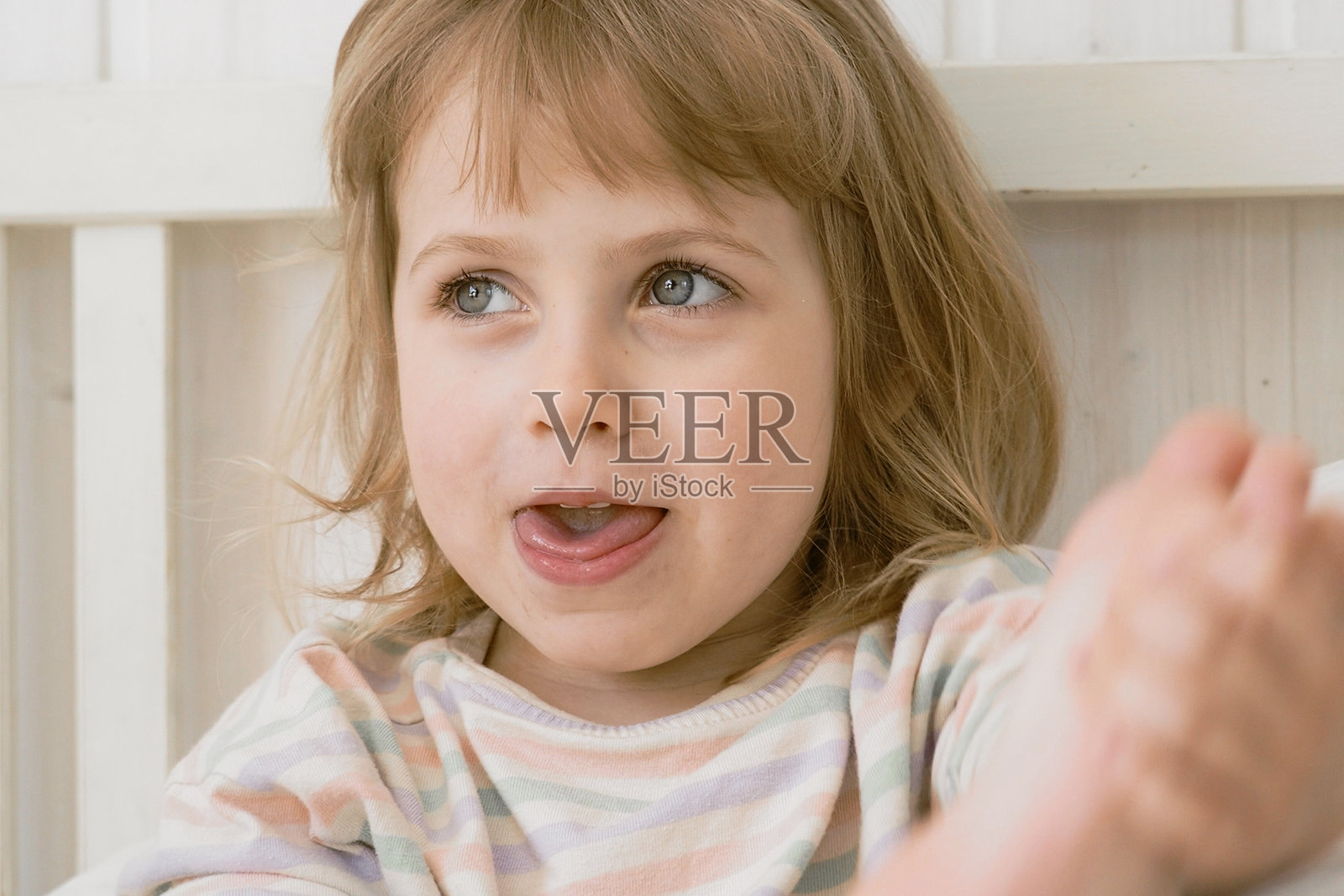 4岁女孩在白墙前做鬼脸，吐舌头，表情滑稽。孩子做表情。近距离面部特写，低对比度，展现孩子疯狂滑稽的姿态，充满趣味的愚蠢肖像。照片摄影图片