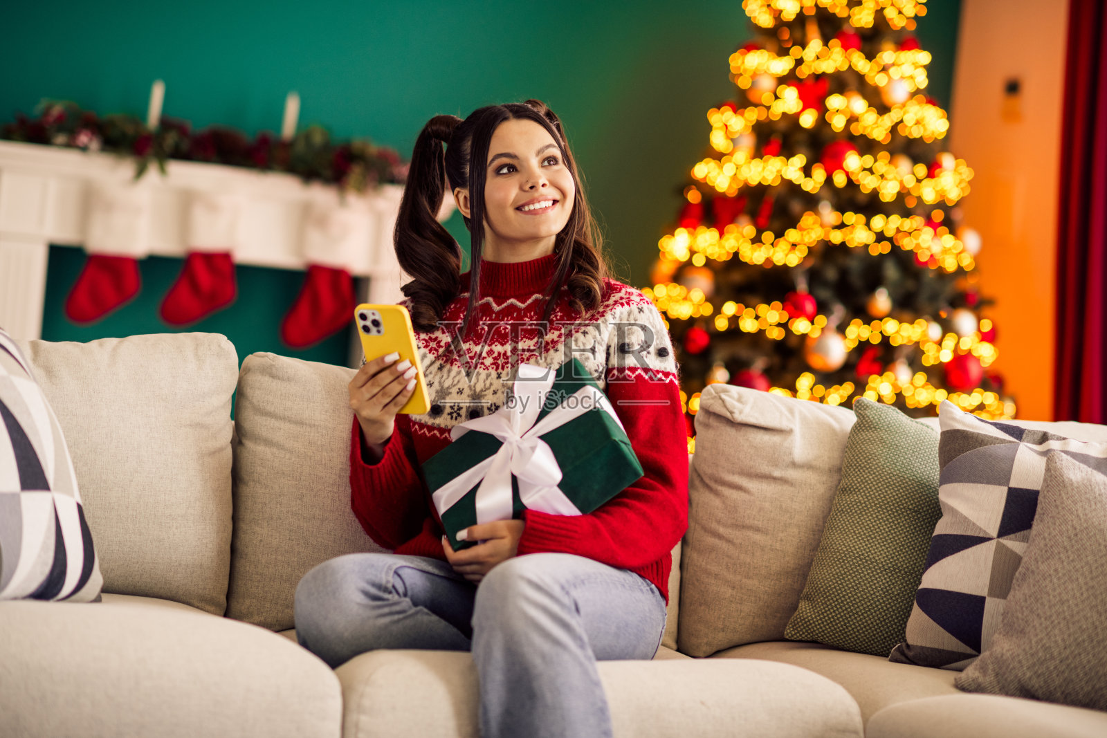 年轻女子在温馨的圣诞装饰背景下，手持手机和礼物，享受着节日的喜悦。照片摄影图片