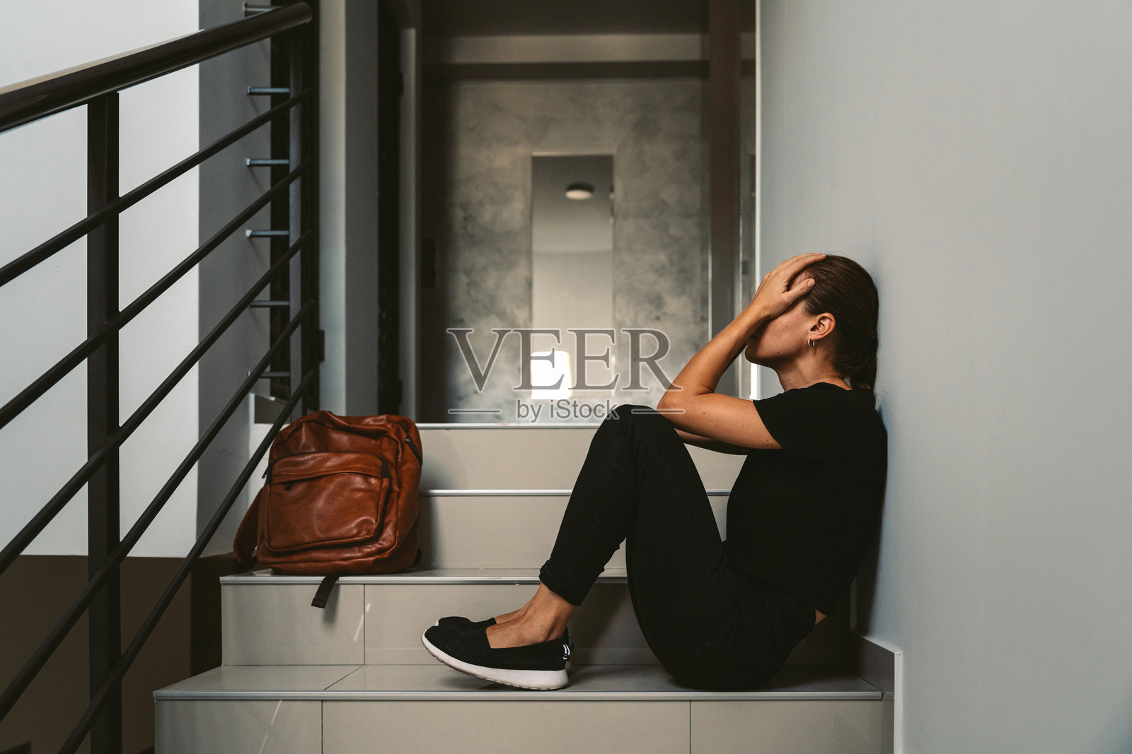 一名沮丧的女子坐在楼梯间，双手捂着脸。照片摄影图片