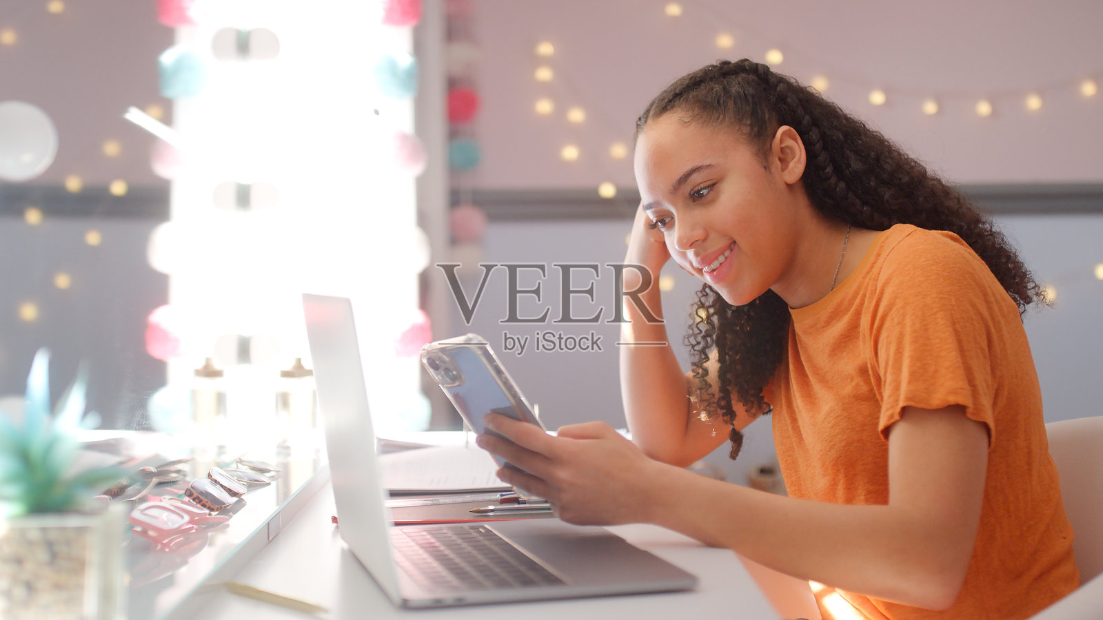 少女在家卧室里用笔记本电脑学习，同时看着手机。照片摄影图片