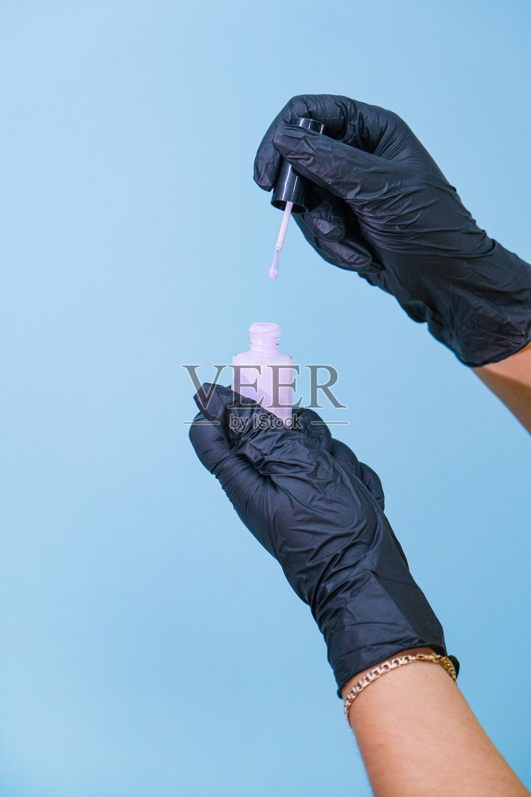 戴着手套的女性双手拿着紫色指甲油瓶，背景为蓝色。照片摄影图片