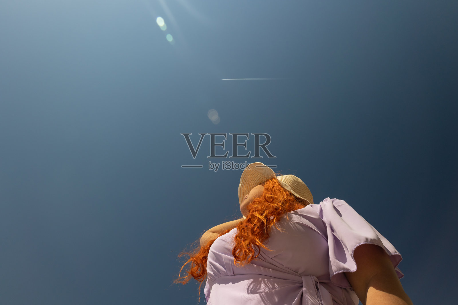 夏日戴着草帽的红发女子在晴天仰望天空，低角度拍摄照片摄影图片