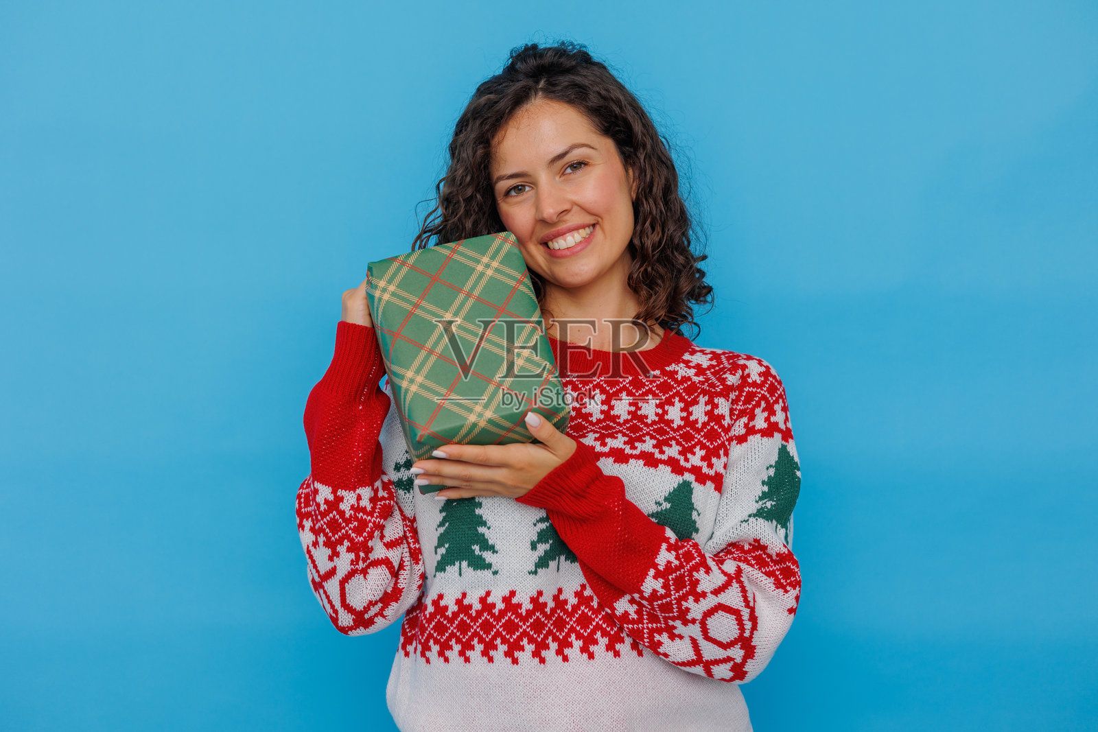 身穿节日毛衣的快乐年轻女子在蓝色背景上收到圣诞礼物，面带微笑，并留有复制空间。照片摄影图片