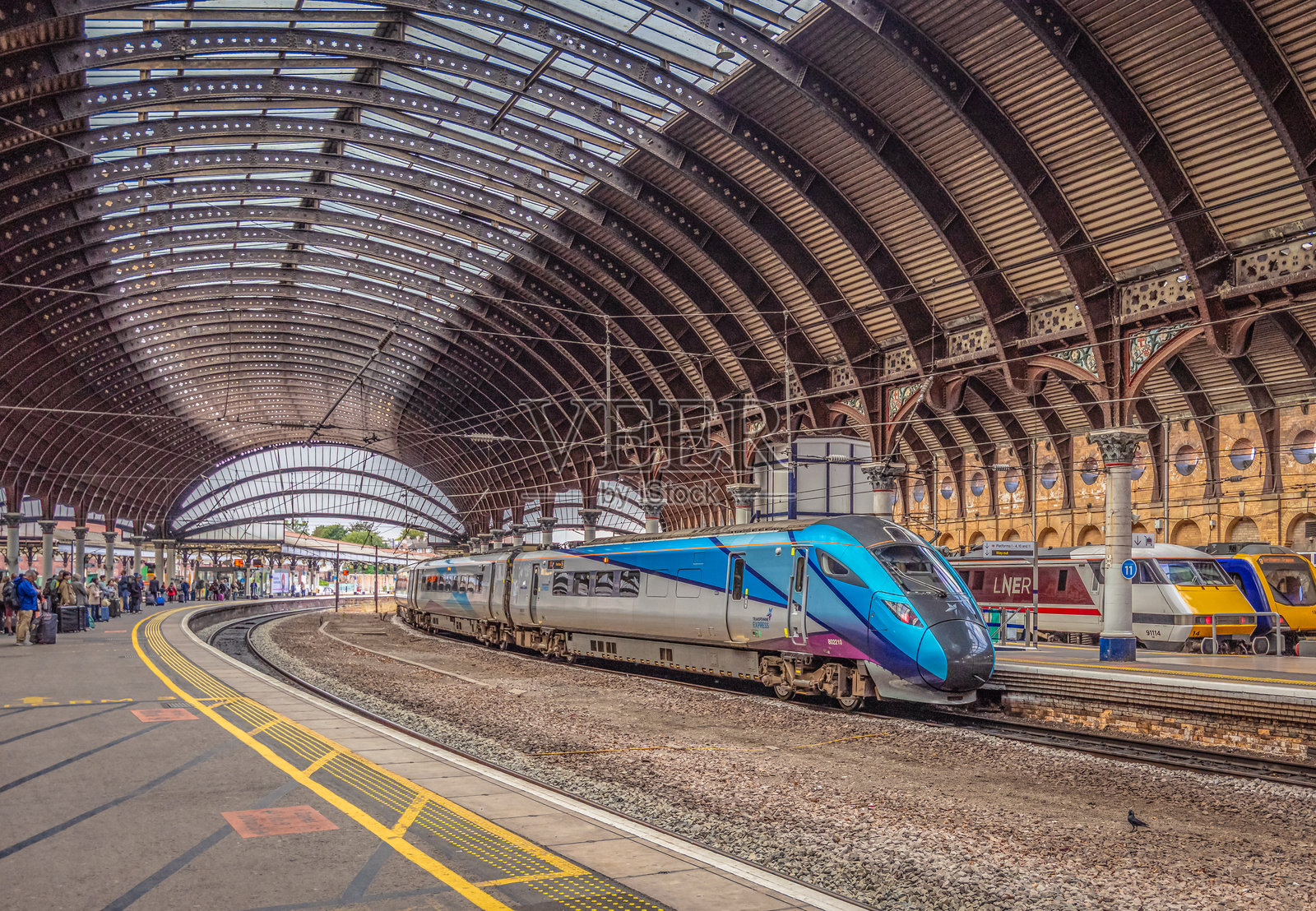 一列火车停在火车站台旁，旁边有柱子和铁制顶棚。照片摄影图片
