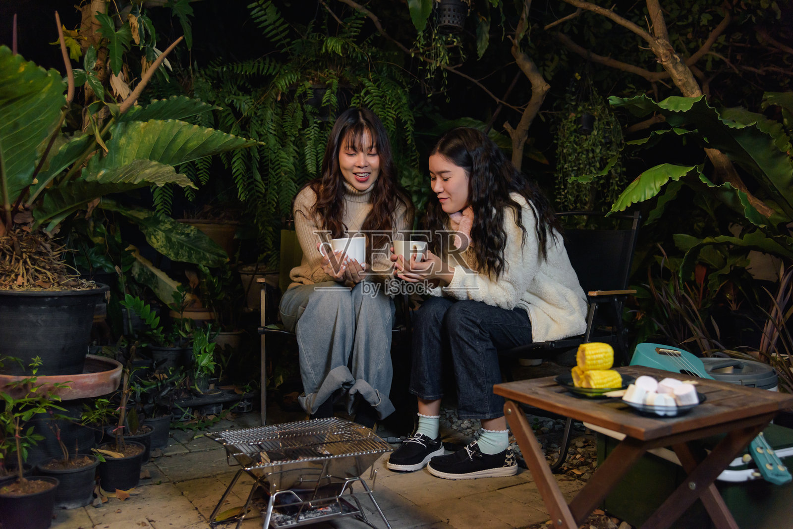 冬季户外营地，开心的女性朋友们在茂密的森林里分享热饮，享受烤棉花糖的炽热光芒，这是温馨聚会和友谊的完美冬夜。照片摄影图片