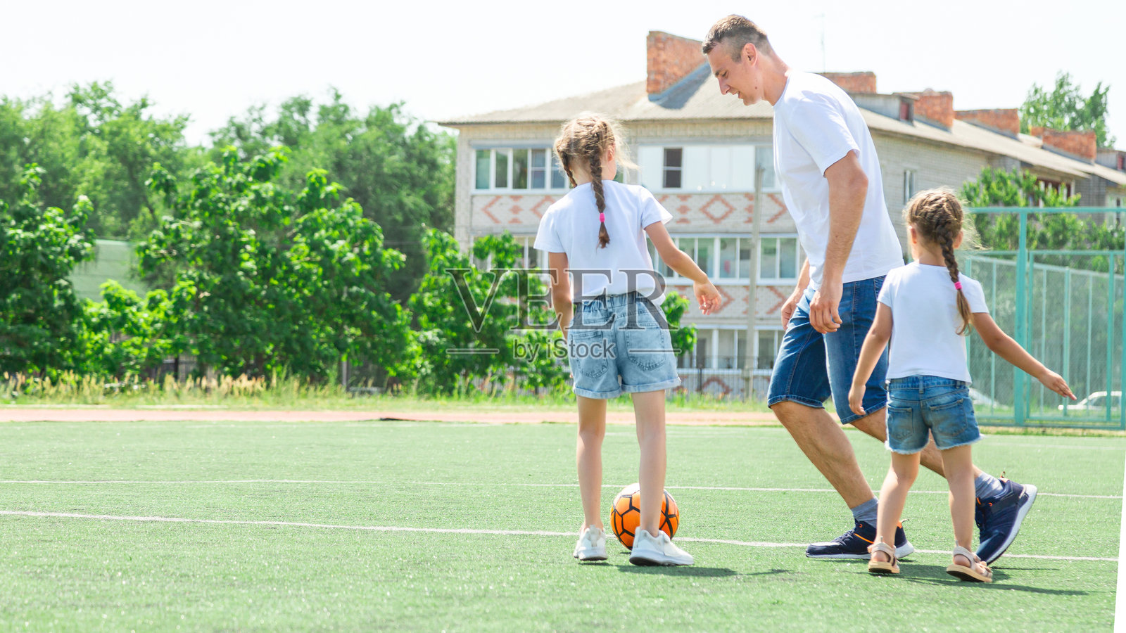父亲和女儿们在踢足球。爸爸和小女孩们在踢足球。年轻活跃的一家人享受阳光明媚的夏日户外时光。健康的儿童运动。足球俱乐部。照片摄影图片