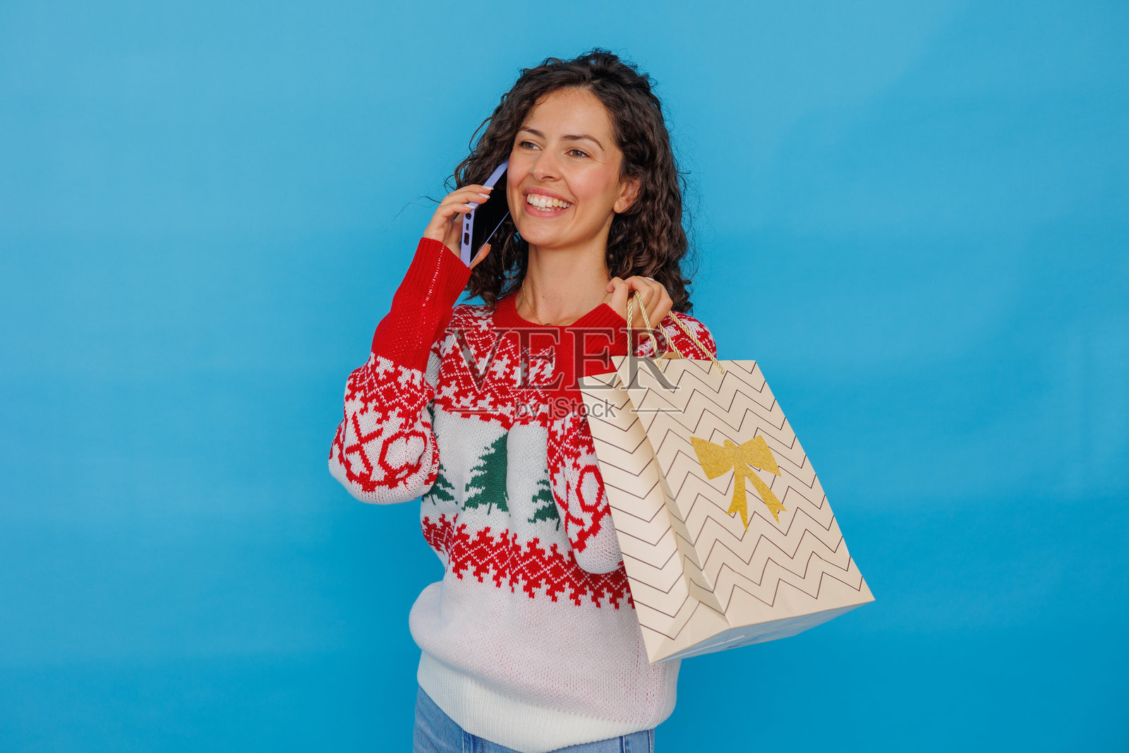 快乐的女人正在打电话，手里拿着购物袋，穿着圣诞时尚庆祝节日。照片摄影图片