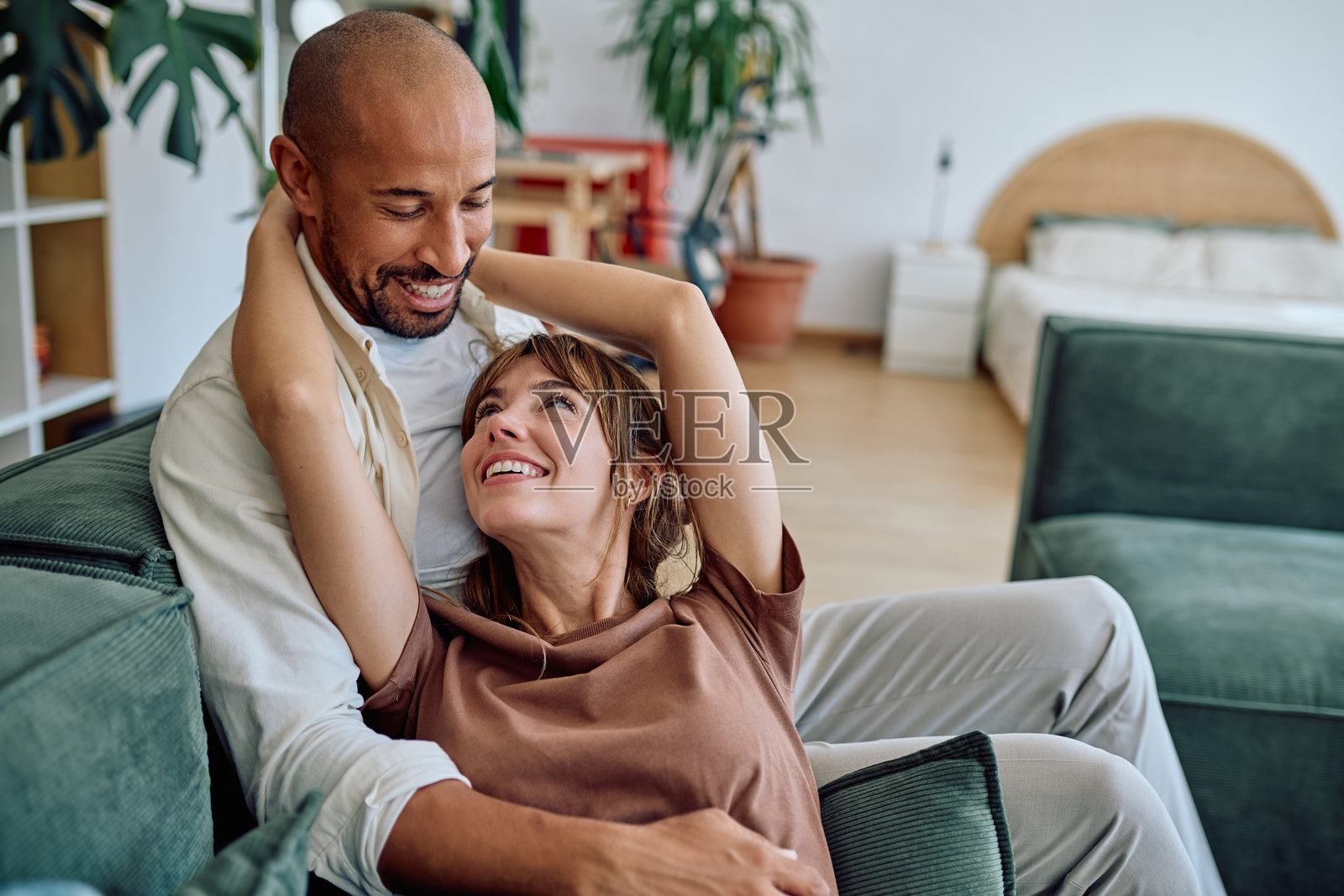 快乐的夫妇在家放松地躺在沙发上，拥抱并微笑。照片摄影图片