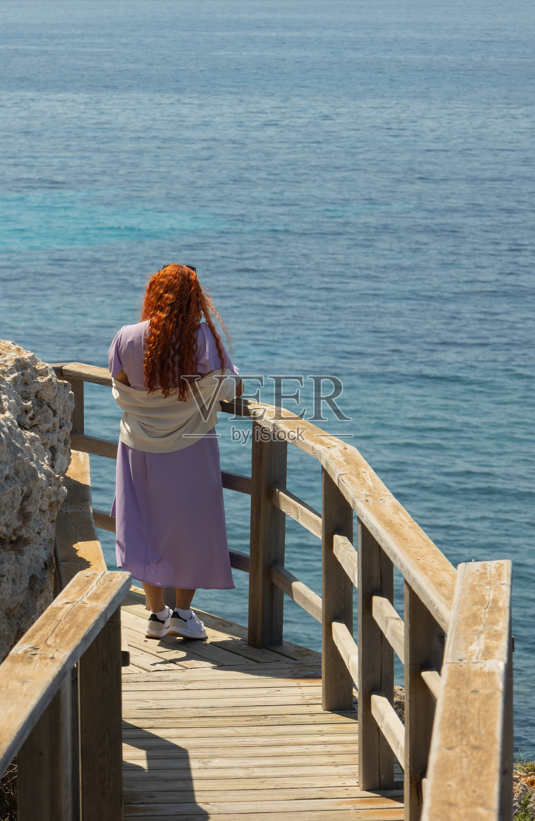 一位红发女子正在一条木制海岸小径上眺望大海照片摄影图片