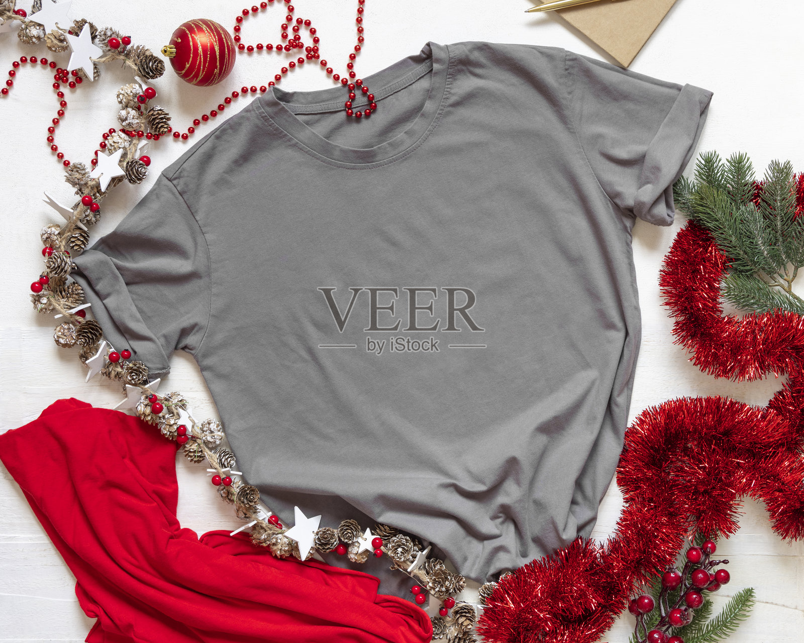 空白的灰色男女皆宜T恤，靠近金色和红色的圣诞装饰品，俯视白色背景，样机照片摄影图片