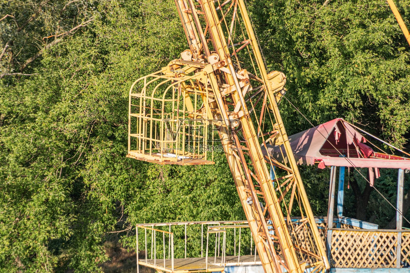 高耸的黄褐色起重机和小型设备组成的工业场景，背景为树木，采用写实风格，强调纹理和结构，色彩对比鲜明，户外环境照片摄影图片