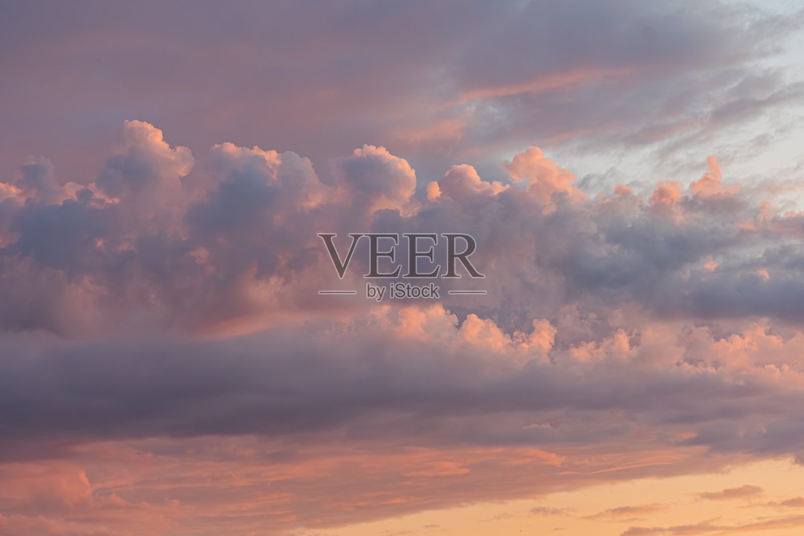 广阔的天空中粉色、橙色和浅蓝色渐变的宁静日落，散布着蓬松的粉色云朵，下方的灰蓝色调暗示着黄昏，没有可辨认的物体或文字，风格独特。照片摄影图片