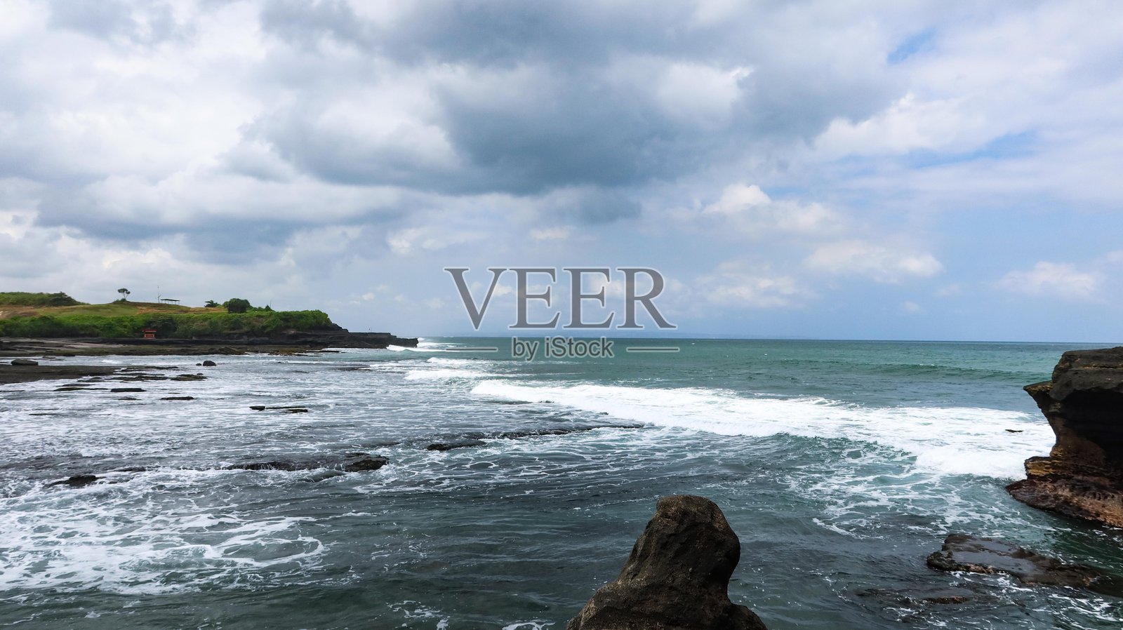 海边的风景，前景是崎岖的岩石构造，背景是拍打的海浪和多云的天空照片摄影图片