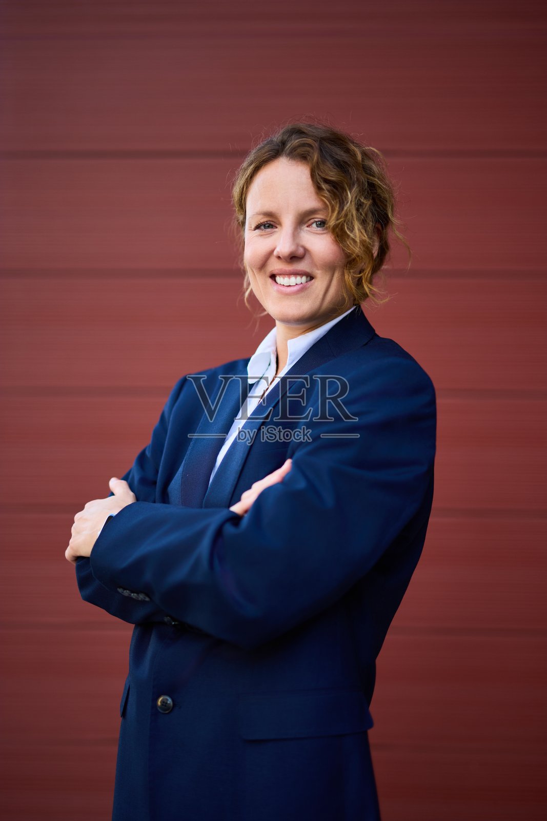 自信的商务女性肖像，身穿海军蓝西装外套，双臂交叉，背景为红色。照片摄影图片