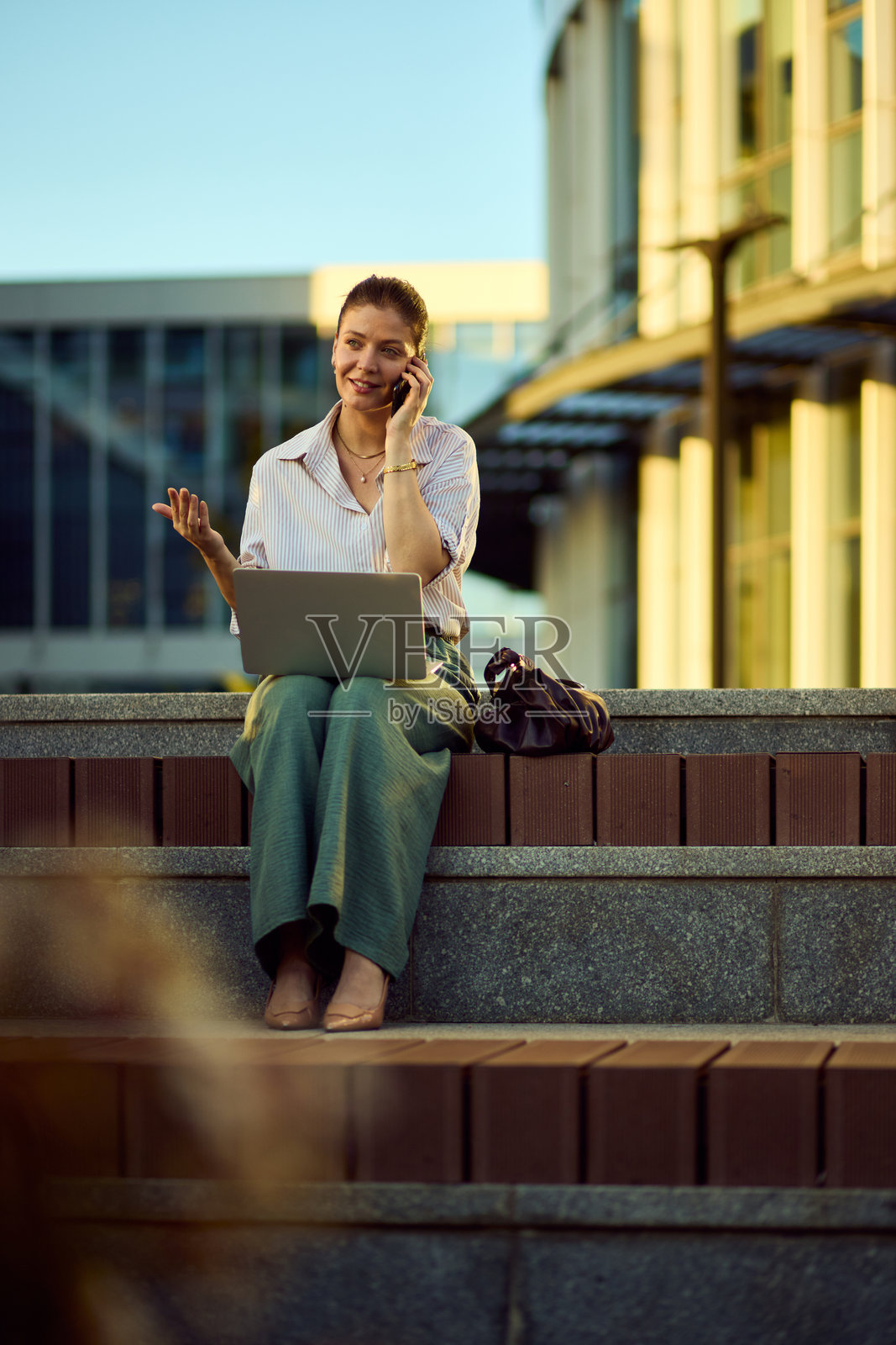商务女性在户外，在城市的台阶上，一边使用笔记本电脑一边打电话。照片摄影图片