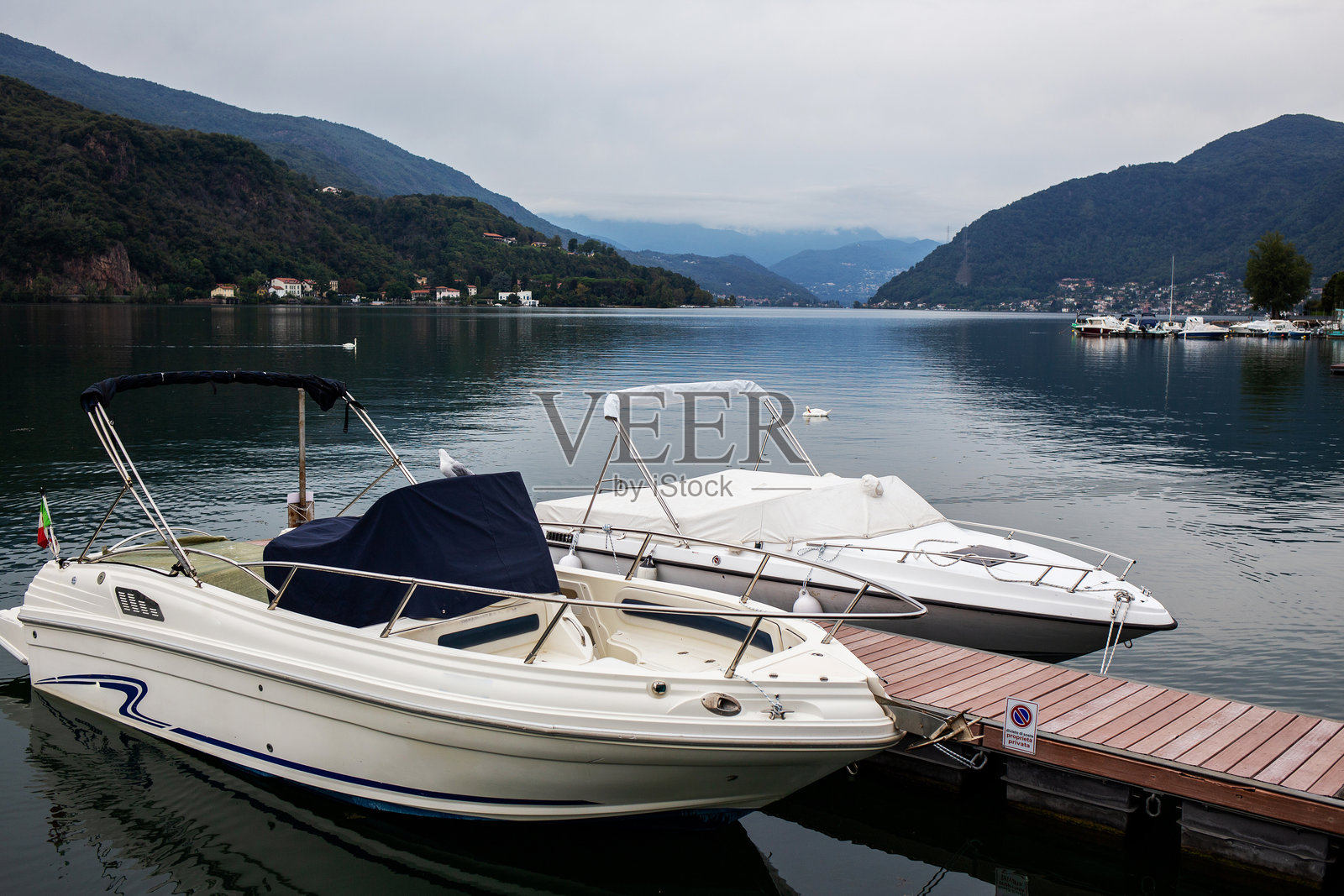 宁静的湖面上停靠着摩托艇，远处是连绵的山峦。照片摄影图片