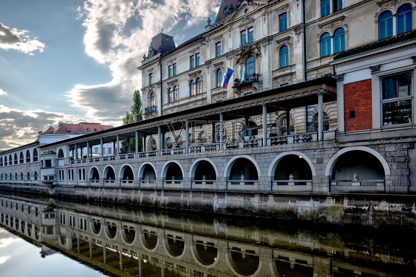 风景如画的卢布尔雅尼察河穿过卢布尔雅那历史中心，两岸绿树成荫，遍布咖啡馆和迷人的河畔建筑。照片摄影图片
