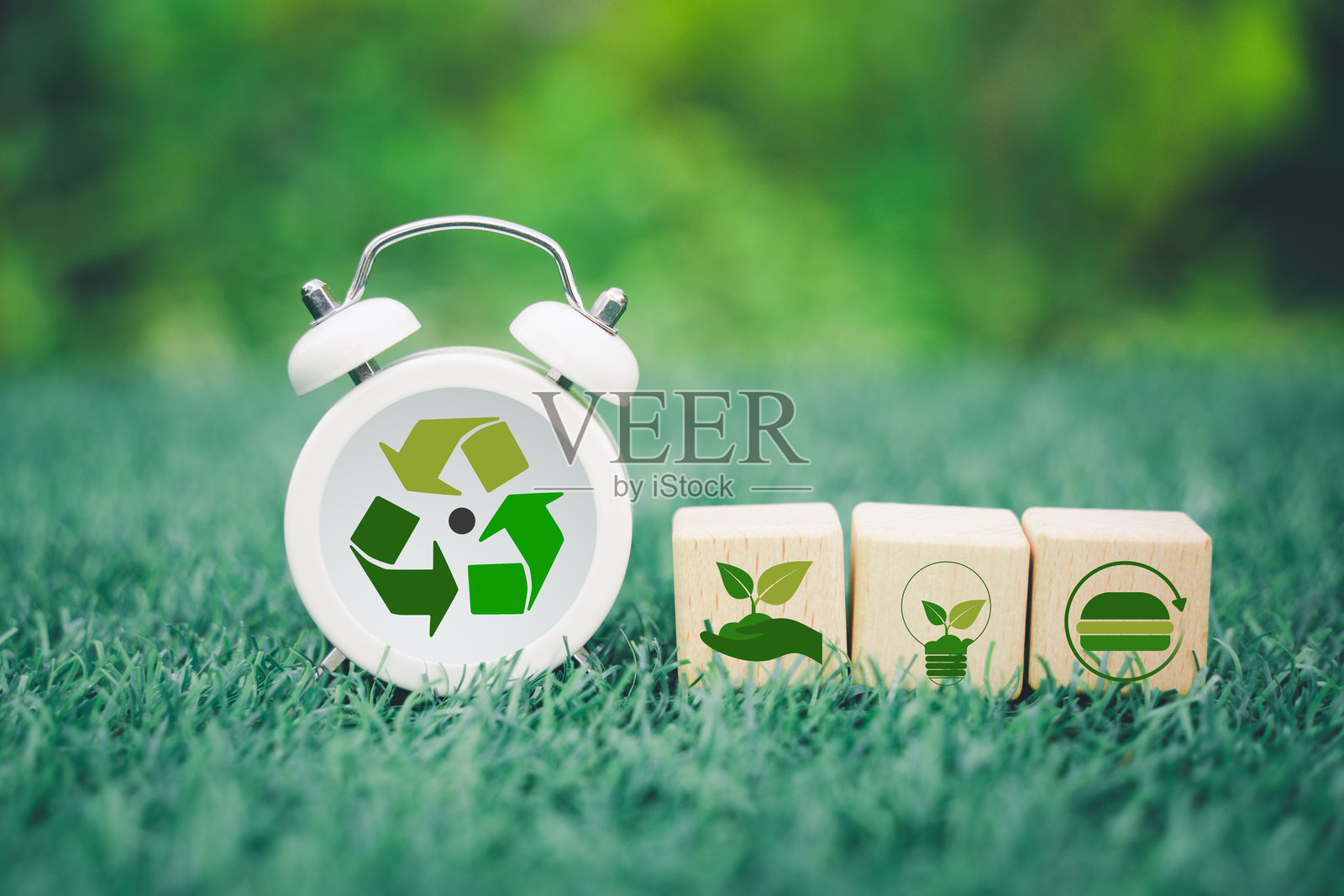 木制立方体和带有回收标志的白色时钟，背景模糊的绿色自然，代表减少碳排放、碳中和概念。净零温室气体排放目标。照片摄影图片