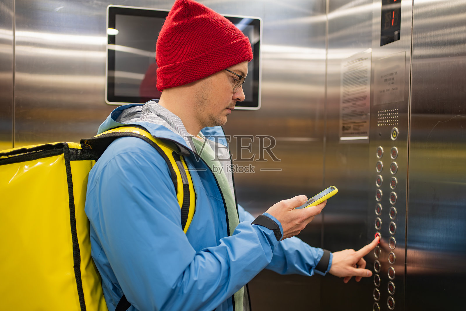 送货员背着黄色保温背包乘坐电梯，在楼层间穿梭时查看智能手机照片摄影图片