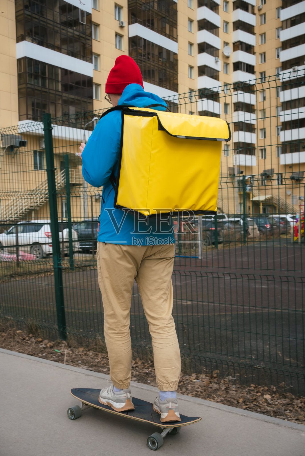 送餐员骑着长板，背着保温箱，使用智能手机查看顾客的在线订单地址，并为顾客送餐。照片摄影图片