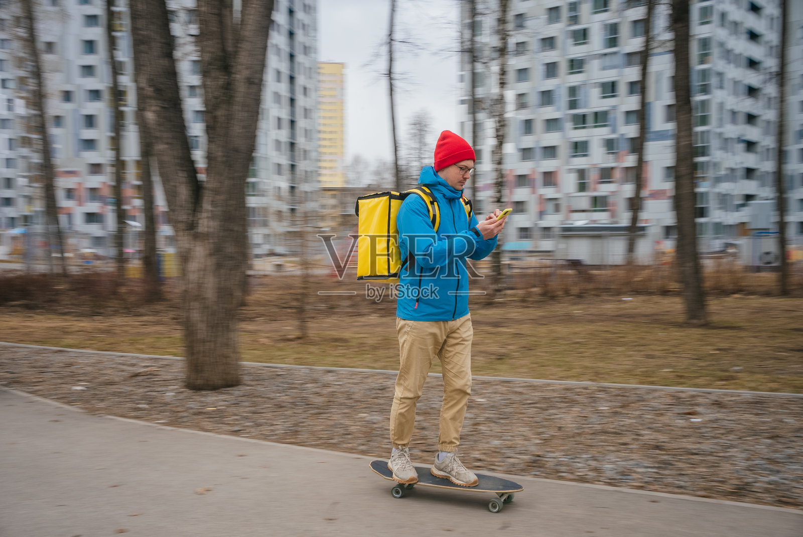 一名快递员在城市公园滑板，身穿黄色保温背包，在运送外卖订单时操作外卖应用程序。照片摄影图片