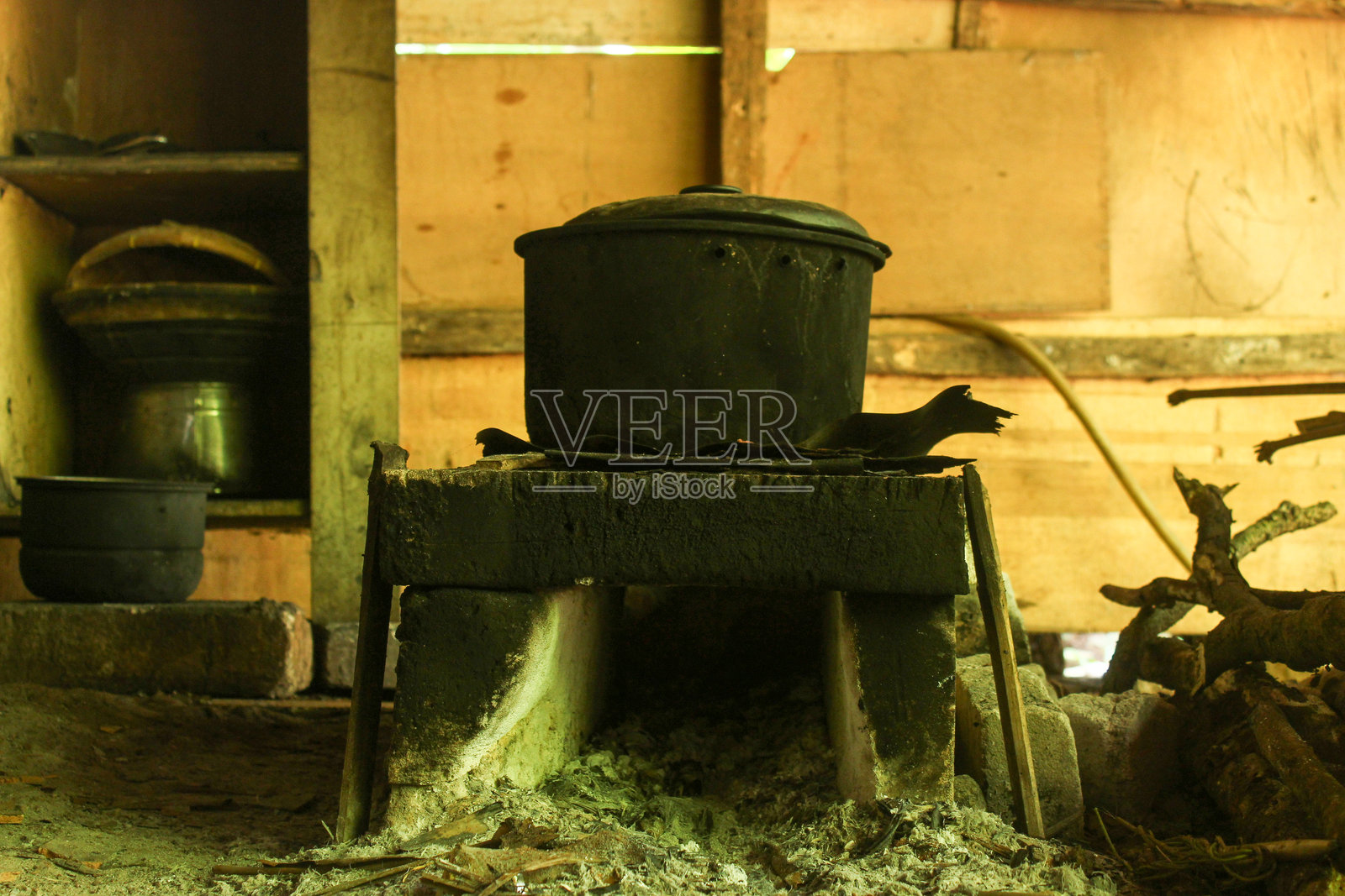 一个用于柴火烹饪的传统砖砌炉灶。炉灶上放着一个带盖的旧黑色铁锅和简单的烹饪用具。照片摄影图片