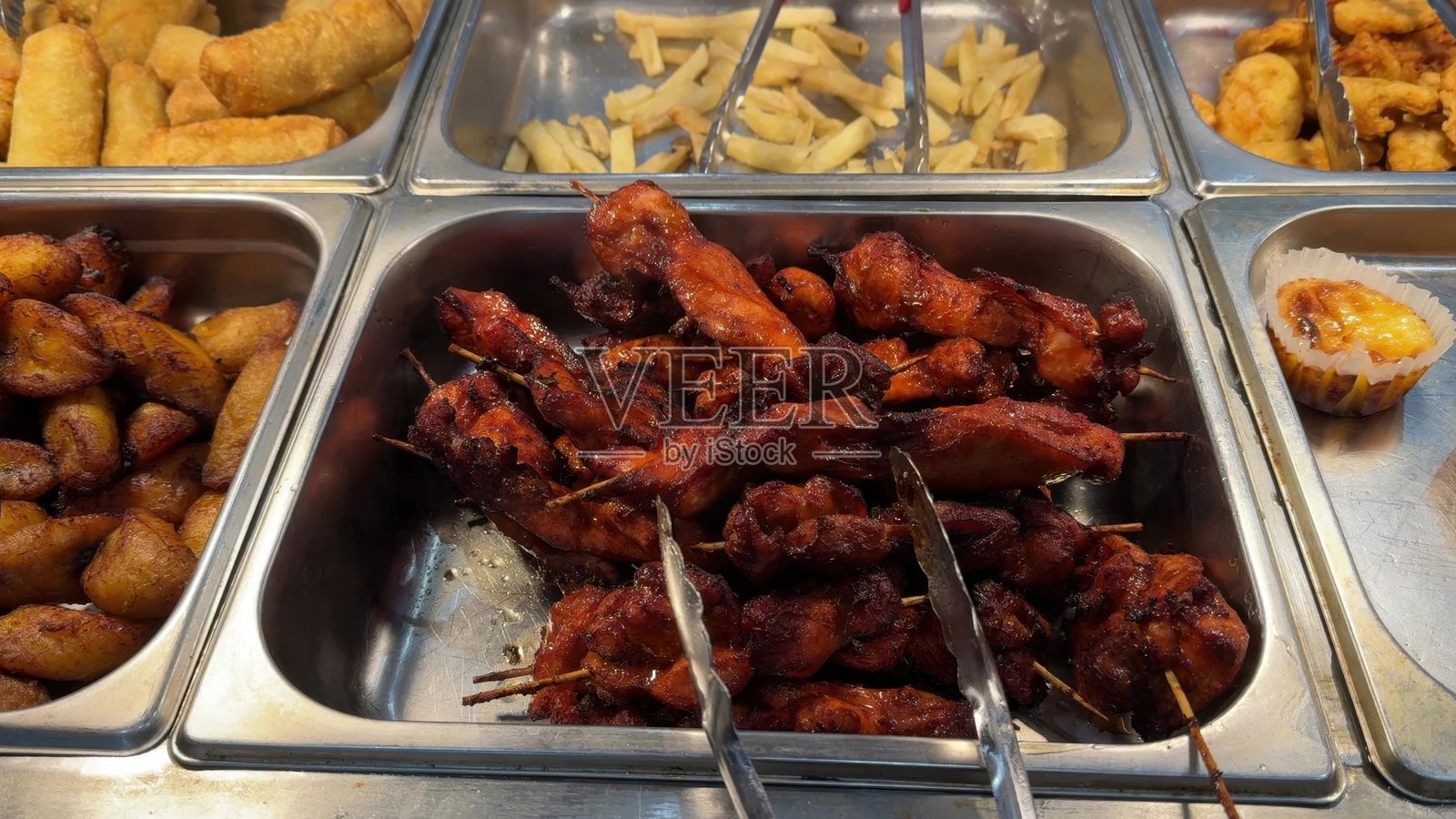 一盘摆满烤鸡肉串的自助餐盘，旁边配有炸芭蕉、炸薯条和春卷。照片摄影图片