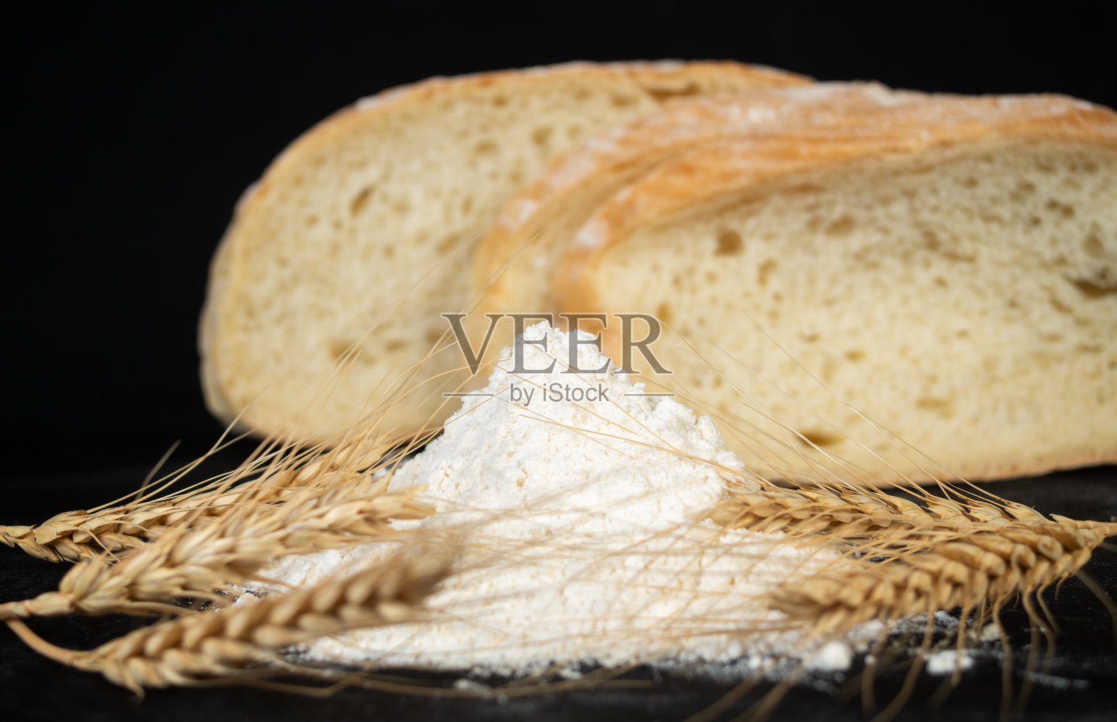 新鲜出炉的面包，配有面粉和麦穗，背景为深色，展现出乡村厨房的氛围照片摄影图片