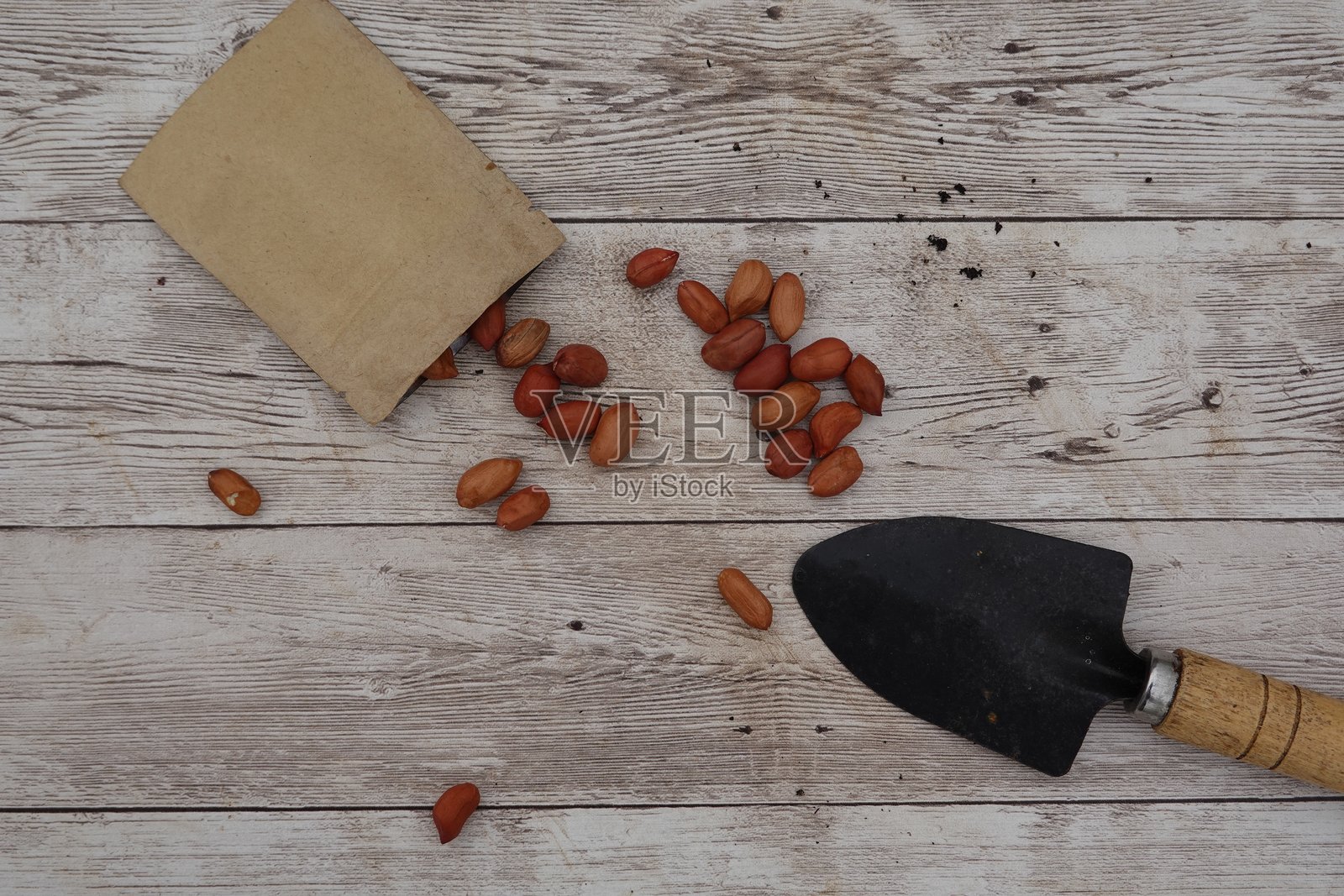 纸袋里的花生洒落在带有铲子的木桌上照片摄影图片