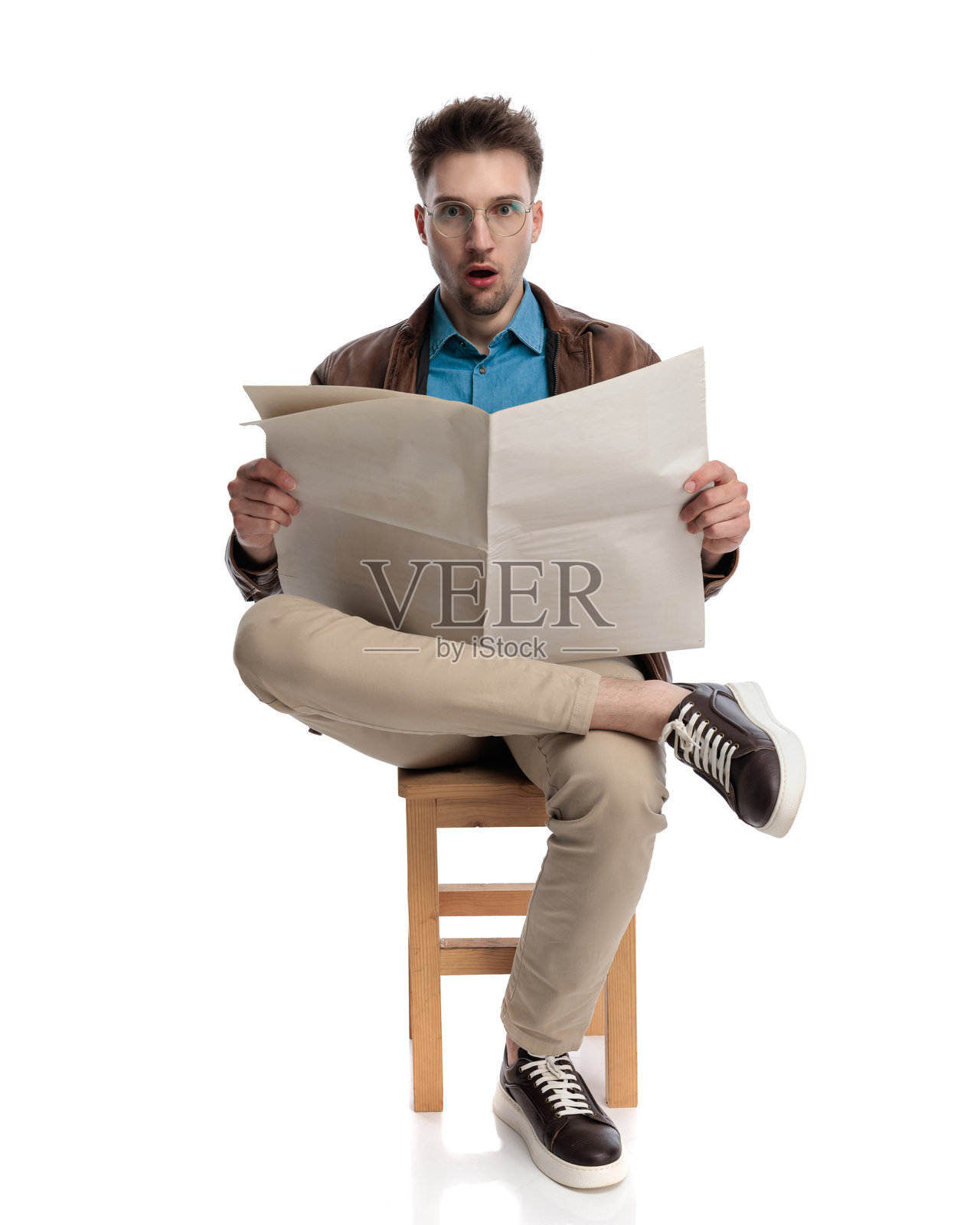 戴眼镜的年轻男子惊讶地读着报纸，感到震惊。照片摄影图片