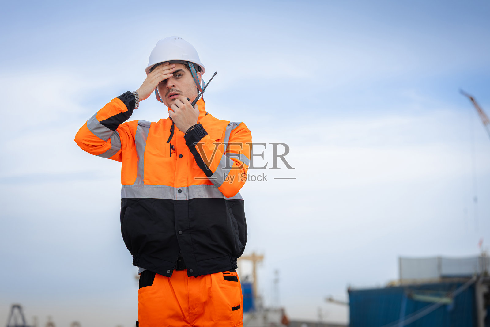 一名担心的工程师正在使用对讲机，一名紧张的港口工人在握着无线电，一名焦虑的建筑经理用手扶着头照片摄影图片