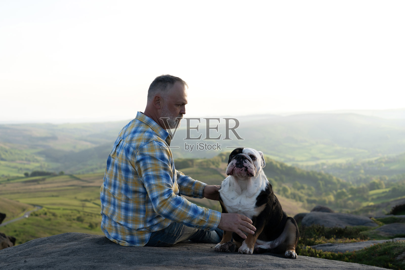 金色的时刻，男人在风景优美的山顶上和斗牛犬享受着美好时光照片摄影图片