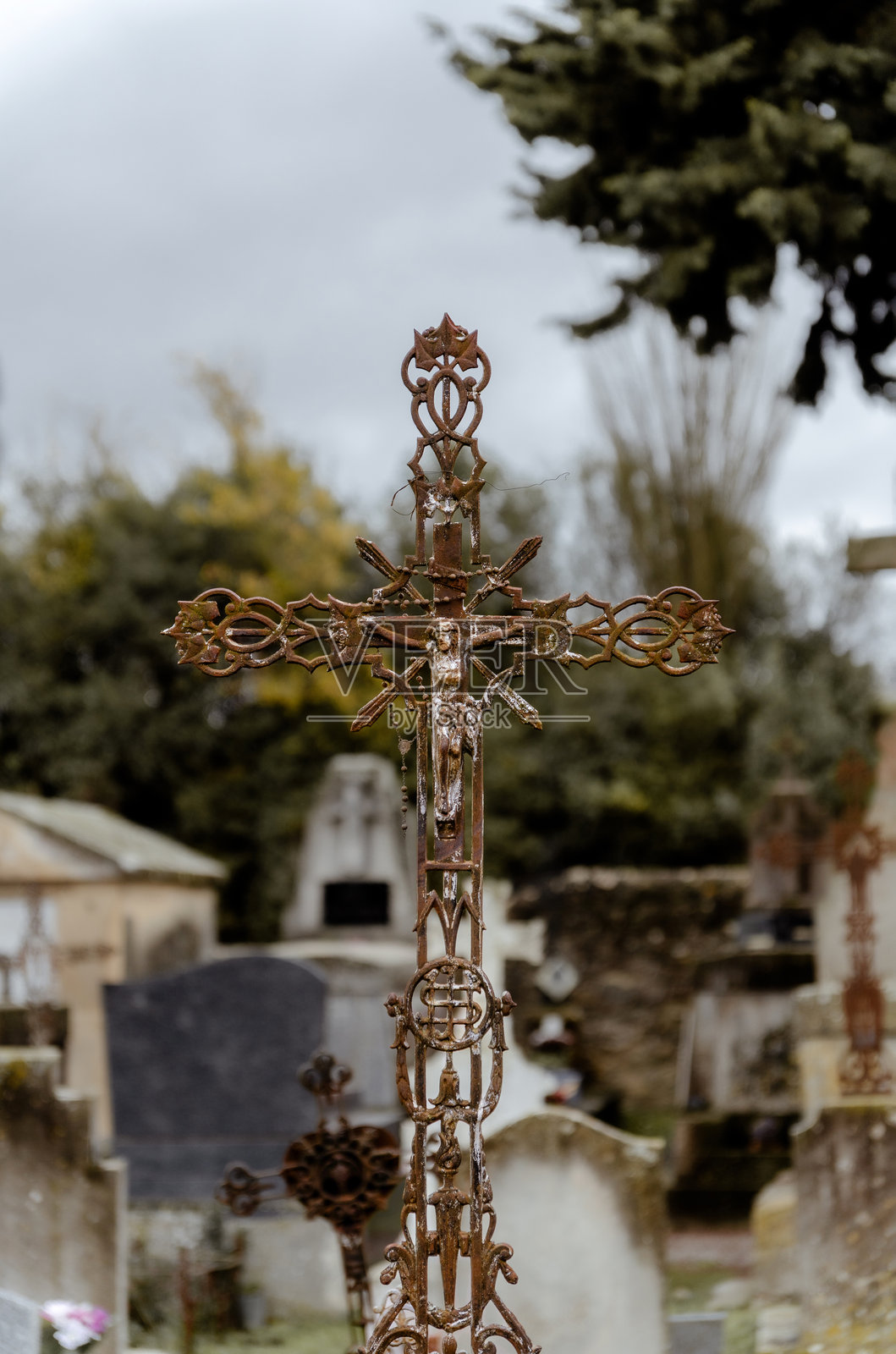 阴天时，在古老的墓地里，一个装饰华丽、锈迹斑斑的铁十字架描绘着被钉在十字架上的基督。照片摄影图片