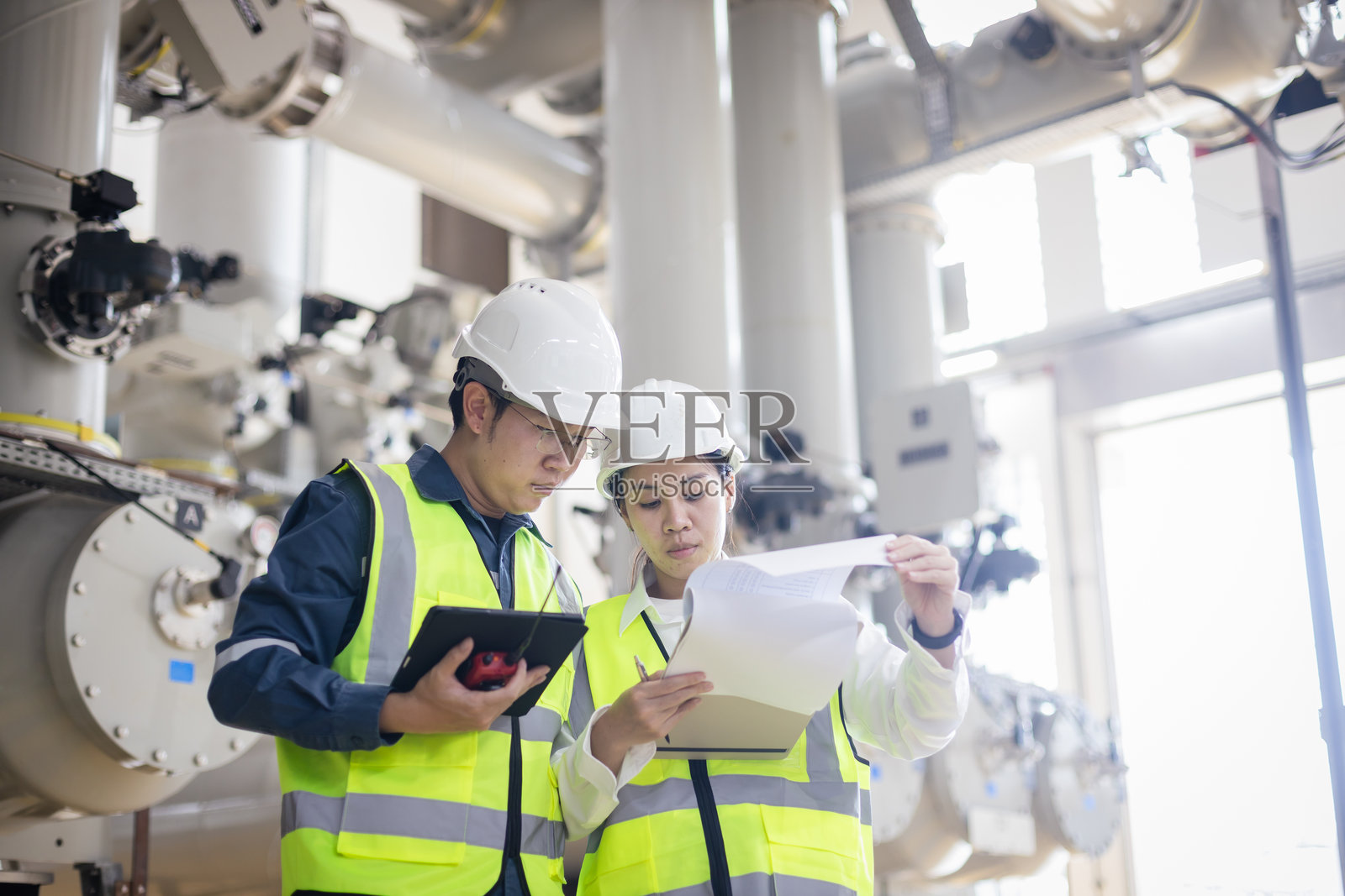 工程师团队在发电站检查高压气体绝缘开关设备（GIS），使用数字平板和报告以确保能源系统的可靠性、安全性以及能源基础设施。照片摄影图片