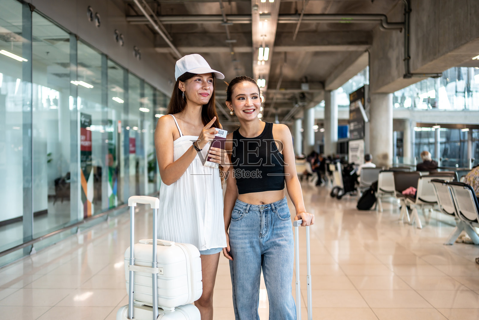 在繁忙的机场航站楼里，两位年轻有活力的亚洲女性正在交谈她们的行程，她们正满怀期待地准备登上飞往现代航站楼的航班。照片摄影图片