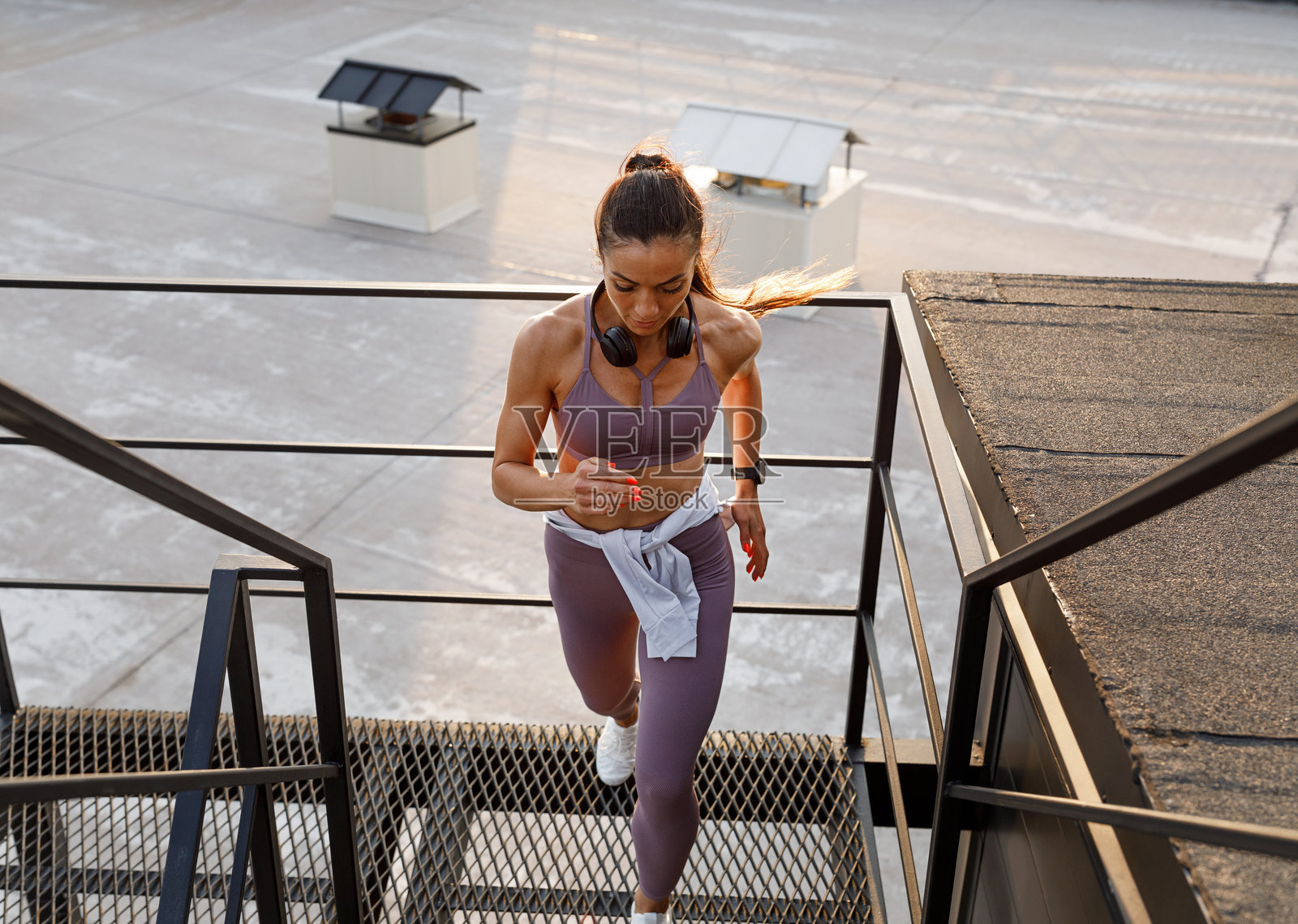 女性健身跑者在屋顶楼梯上奔跑，全身照。身着健身服的女性在屋顶楼梯上跑步。照片摄影图片