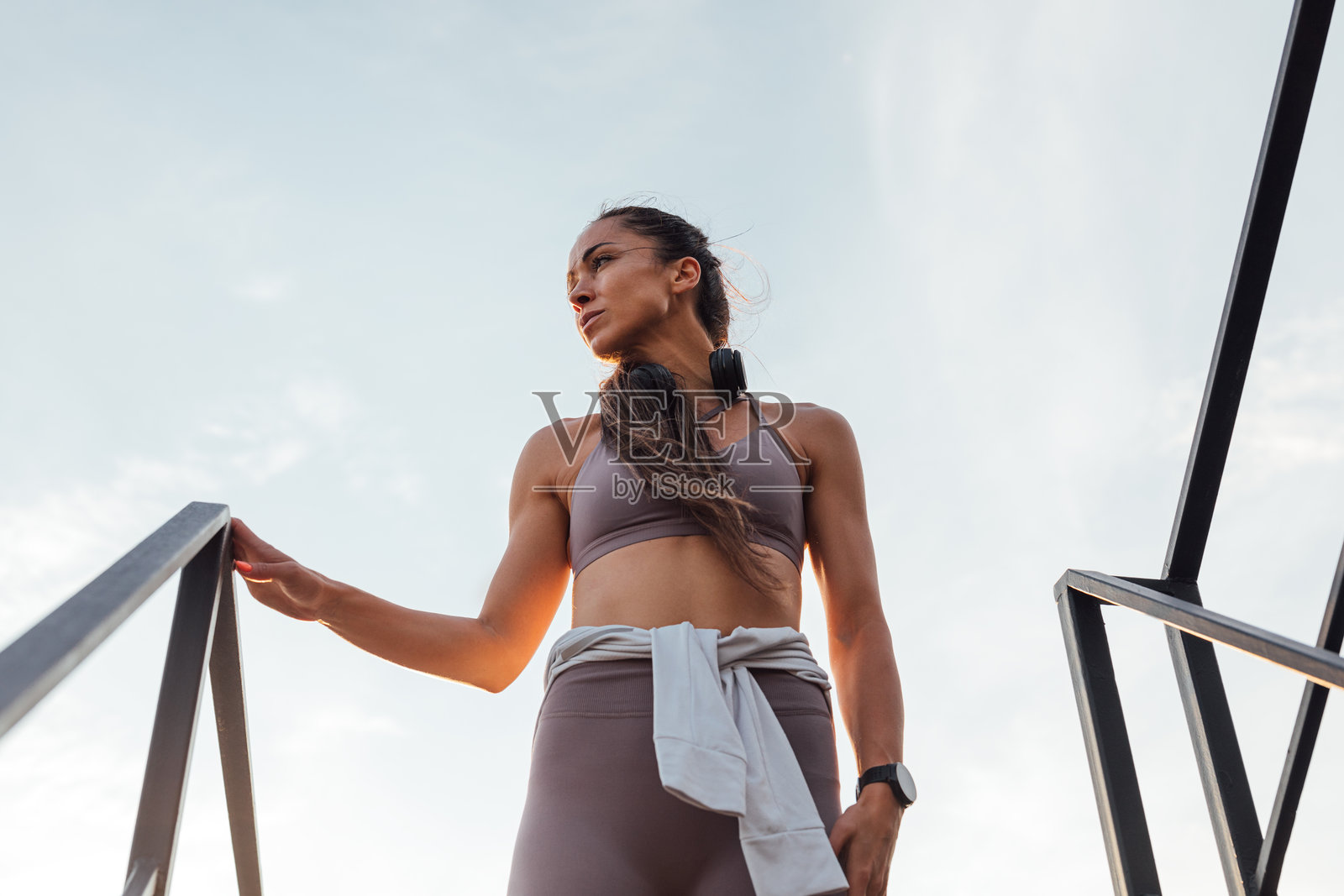 低角度仰拍，身穿运动服的年轻苗条女性站在楼顶楼梯上，望向远方。照片摄影图片