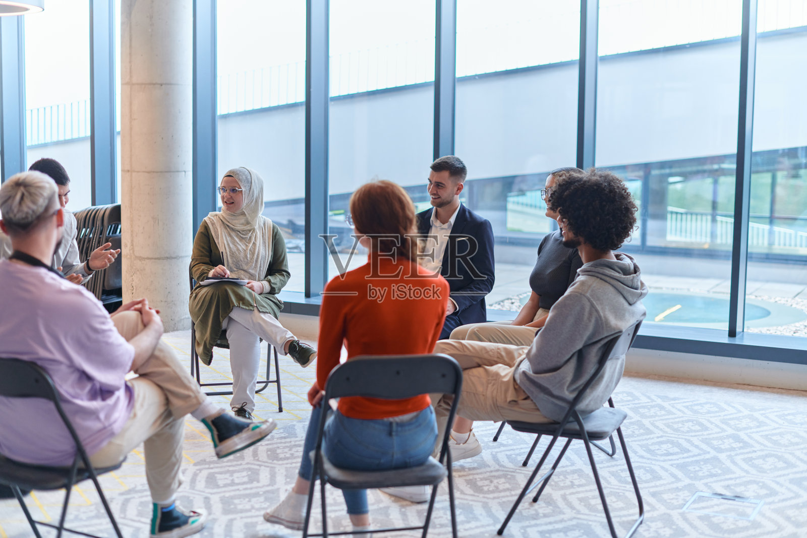一群多元化的年轻企业家围成一圈开会，在大型企业现代化的办公空间内讨论公司面临的挑战和创新解决方案。照片摄影图片