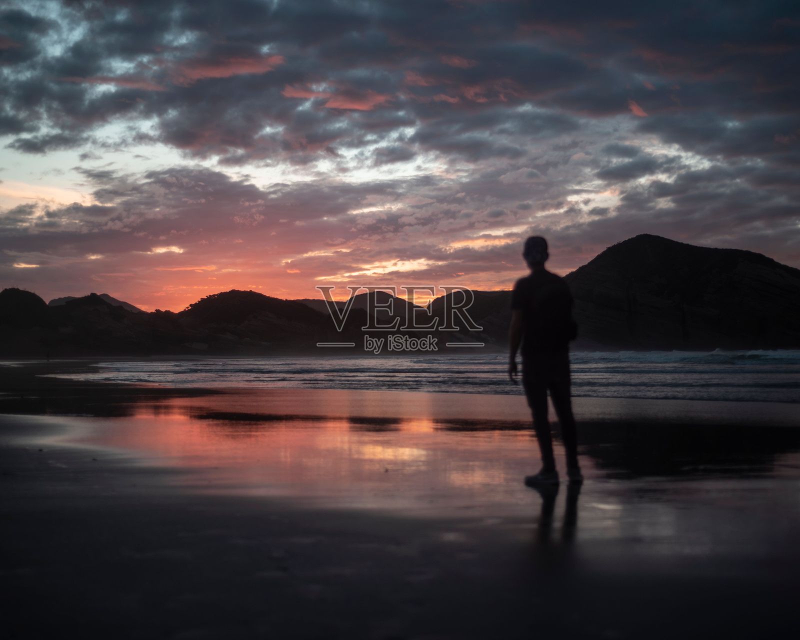 男人站在水边，他的冲浪板在他面前。照片摄影图片
