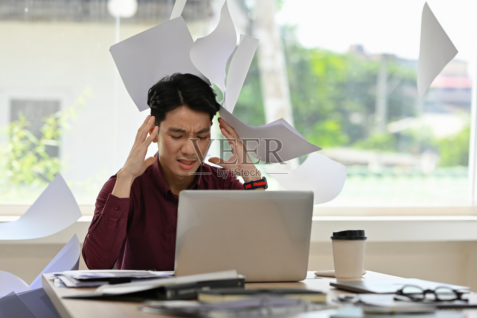 筋疲力尽的商务人士在笔记本电脑前，文件满天飞，表达了工作压力与精神负担，工作压力与办公室倦怠照片摄影图片