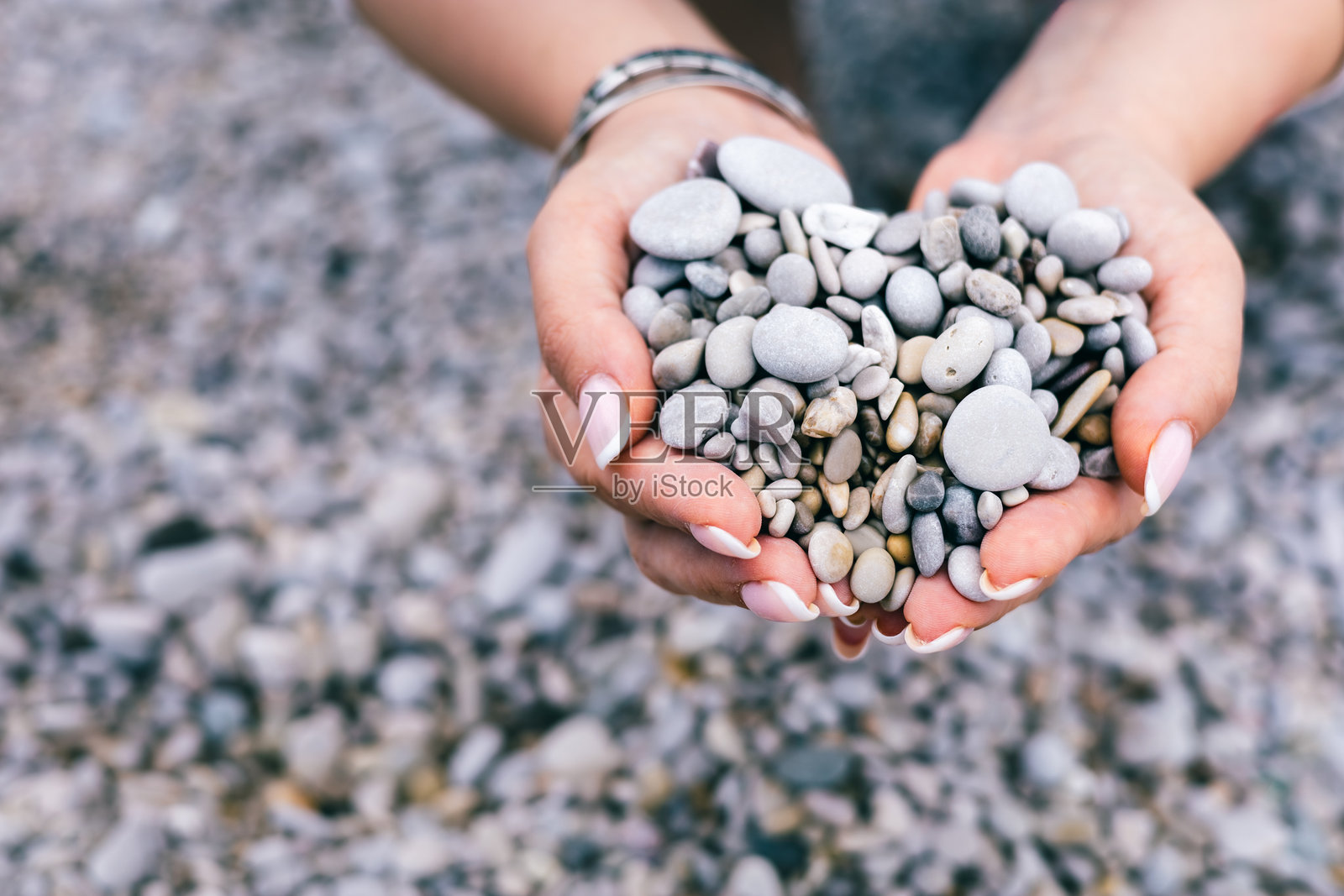 心形鹅卵石在女性手中，背景是岩石海滩，代表着爱、自然与宁静照片摄影图片