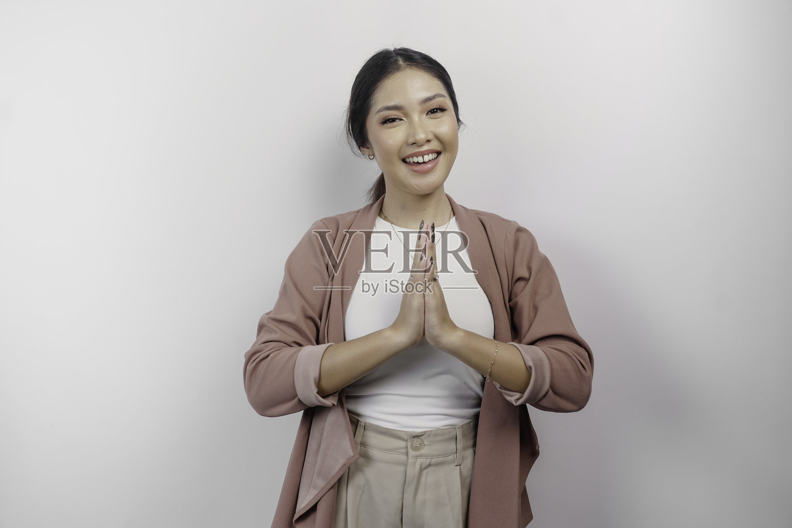 一位面带微笑的年轻亚洲女员工，身穿开衫，正在行传统的问候礼。照片摄影图片